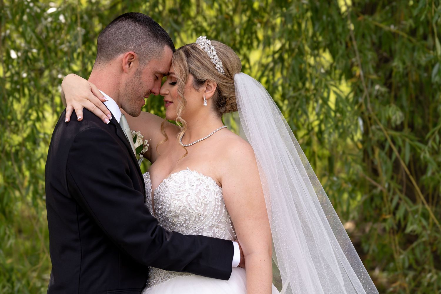 Newlyweds share an intimate moment under a weeping willow tree.