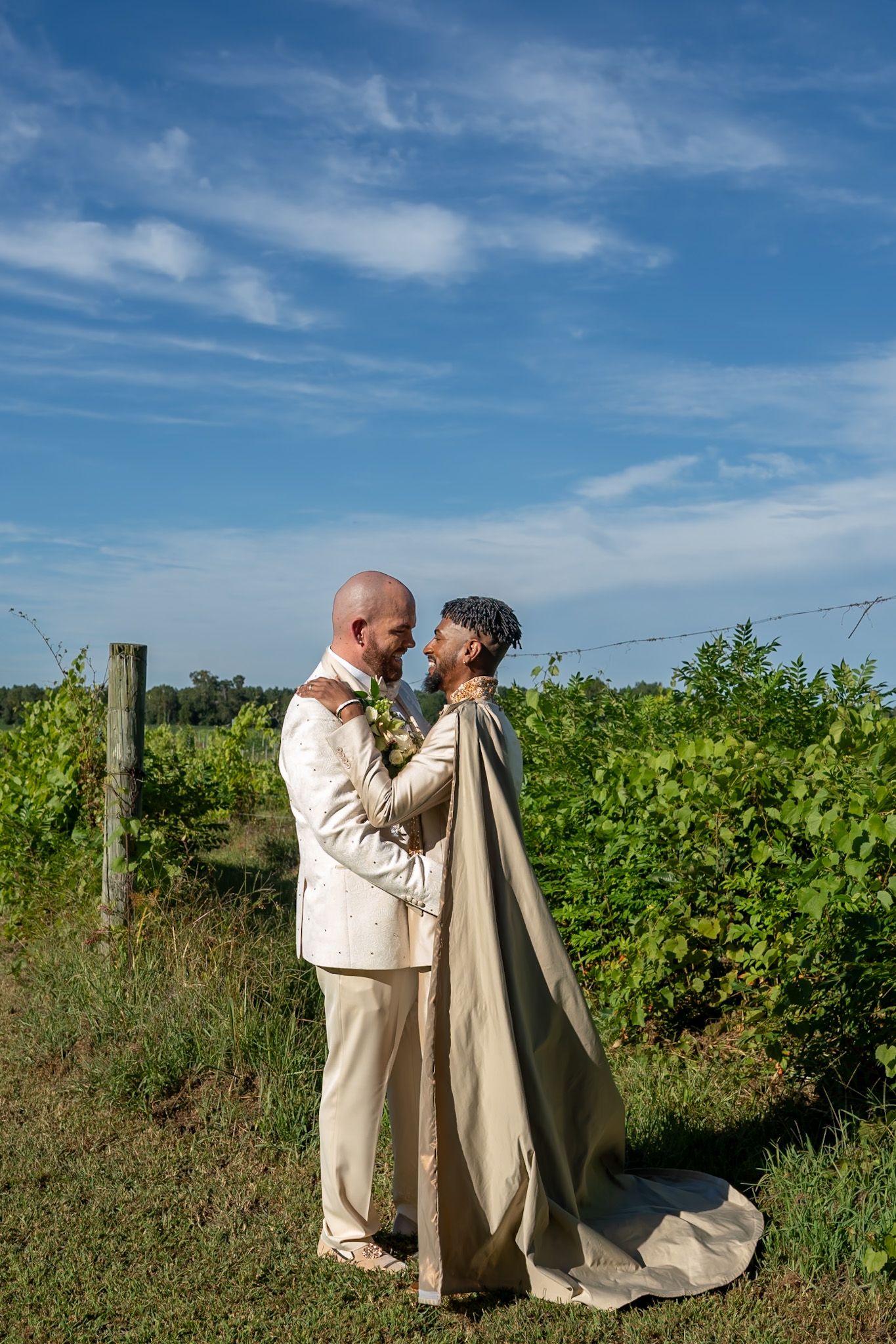 A couple shares an intimate moment in a sunny vineyard with blue skies overhead.