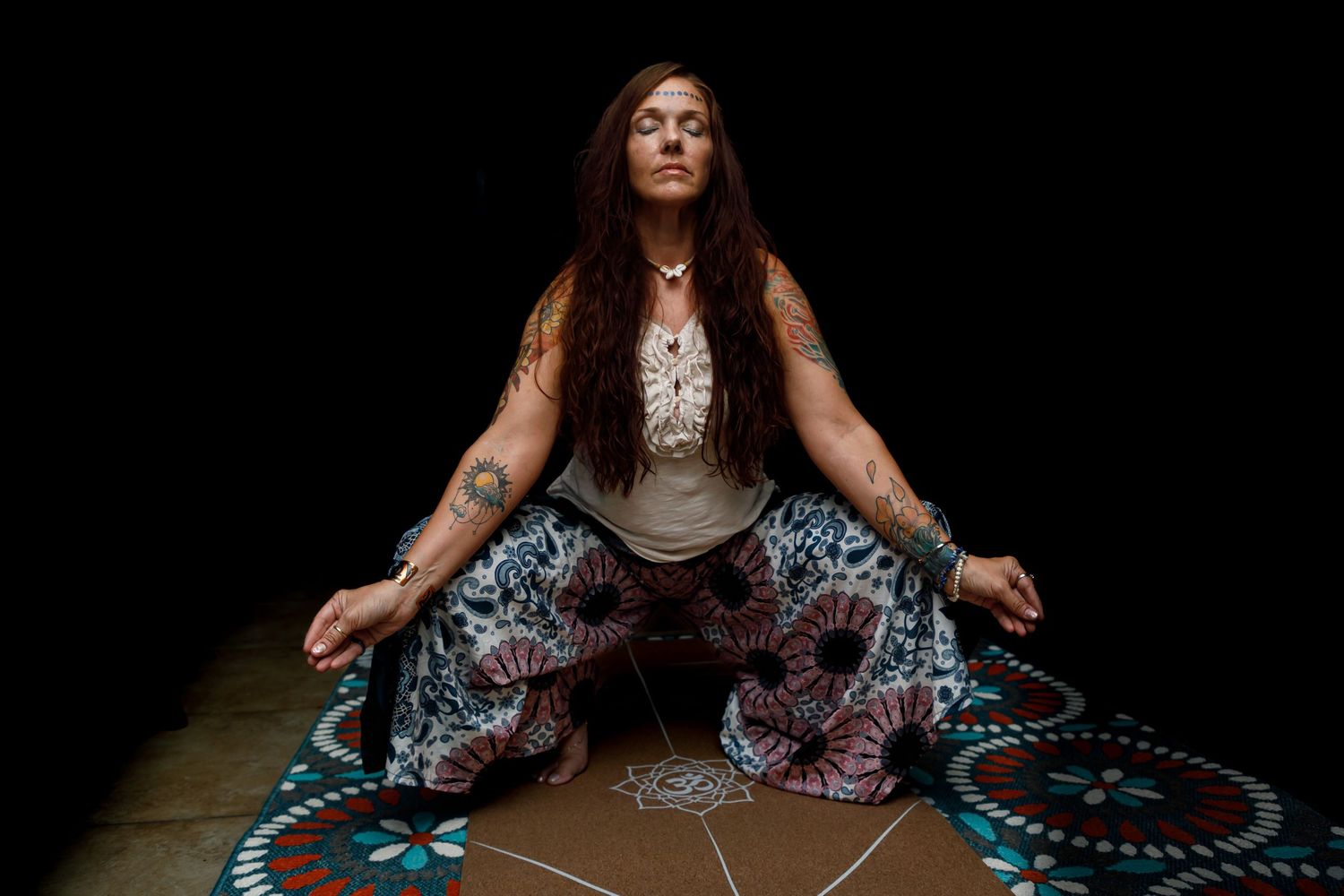 Person seated in lotus position on dark floor with circular patterns.