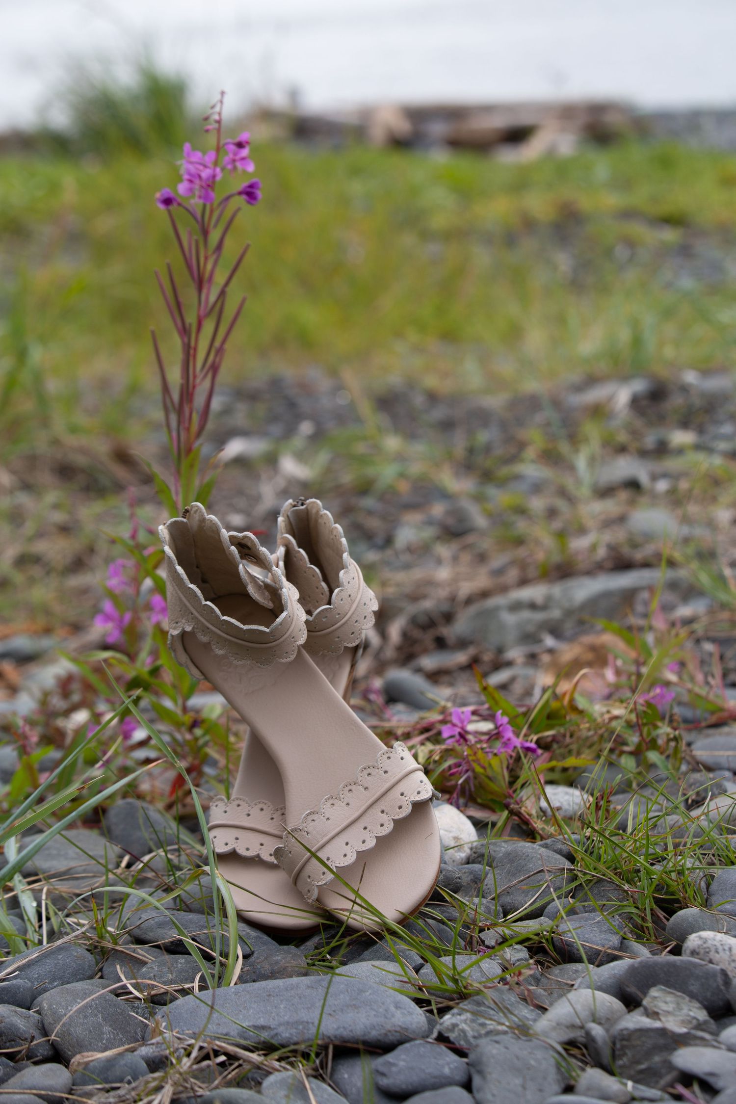 Beige wedding shoes among purple wildflowers and rocks in natural setting.