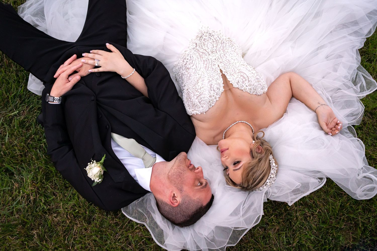 Newlyweds lying on grass sharing a relaxed moment during their wedding photoshoot.
