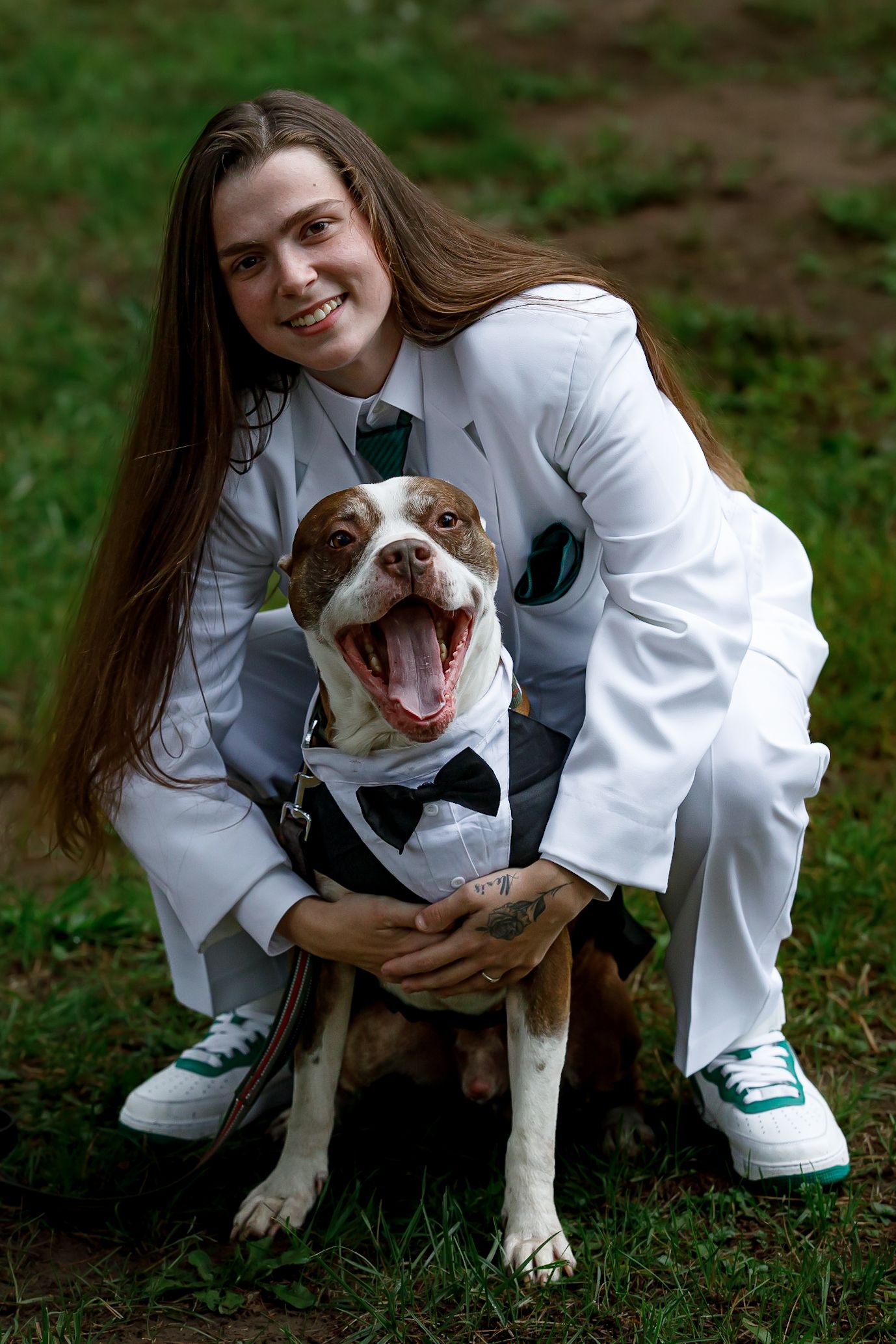 Happy pit bull wearing a bowtie poses with wedding party member in white suit.