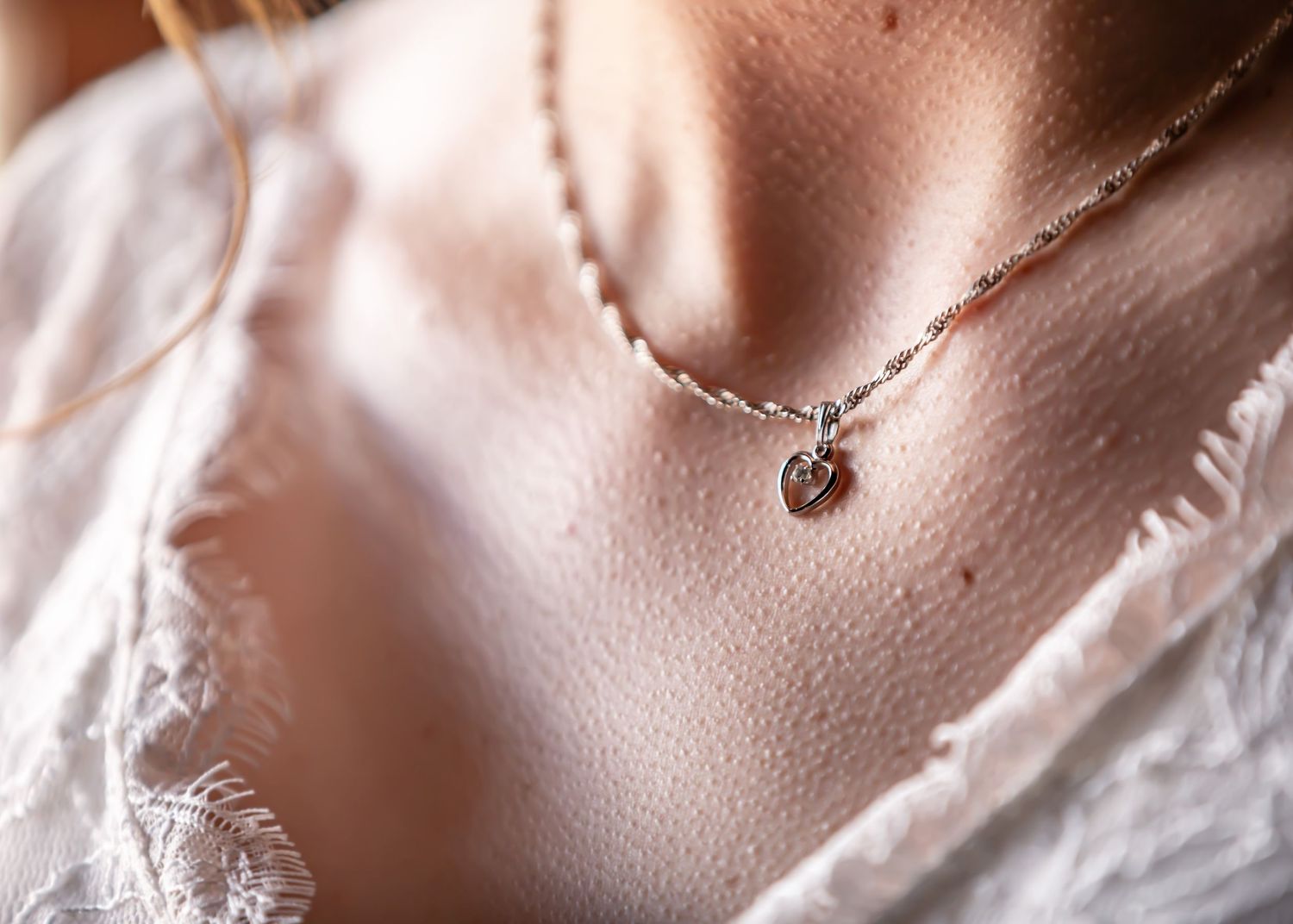 Delicate silver necklace with heart pendant worn with white lace dress.