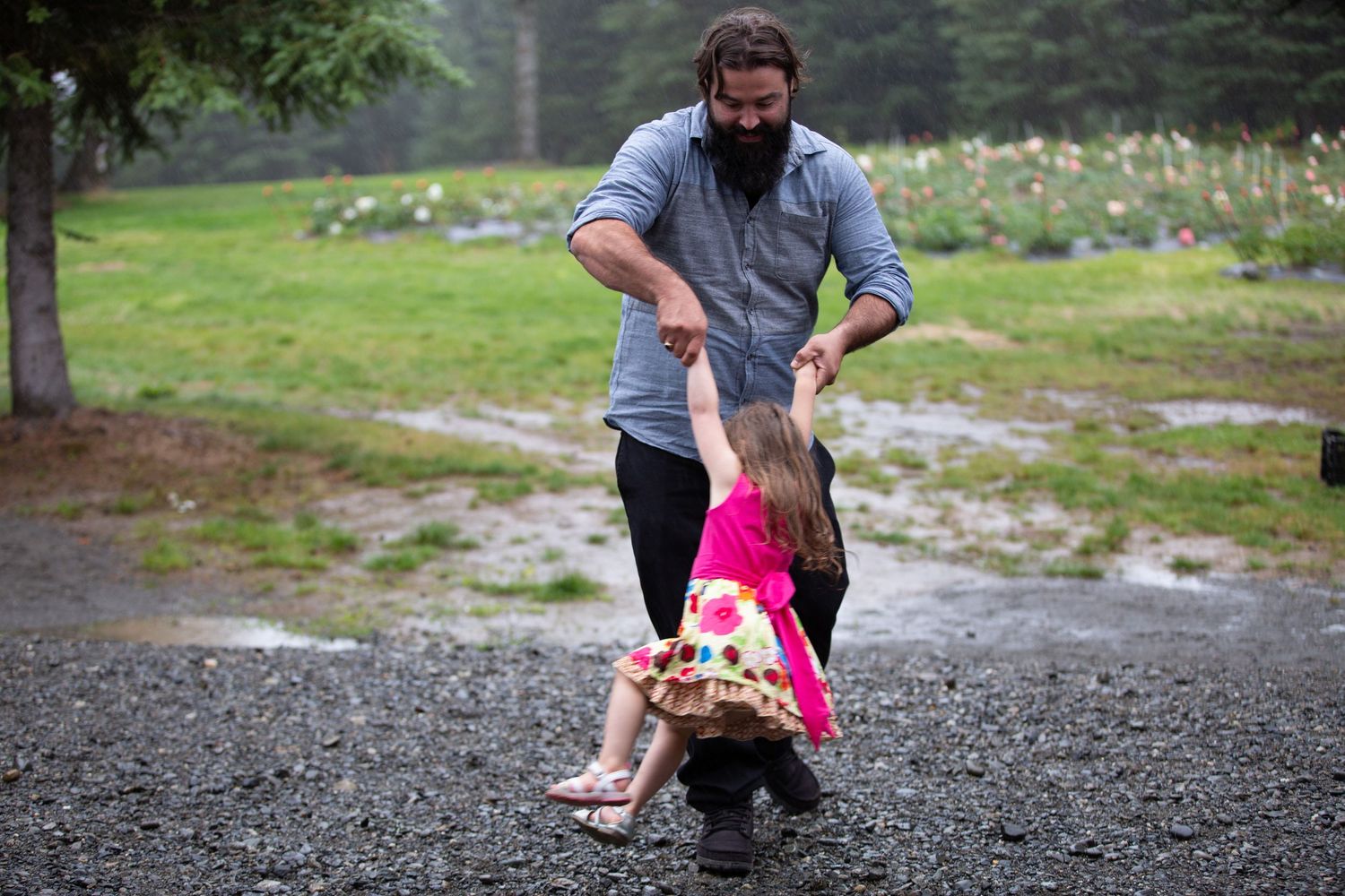 Adult playing with child on gravel path near flower garden.