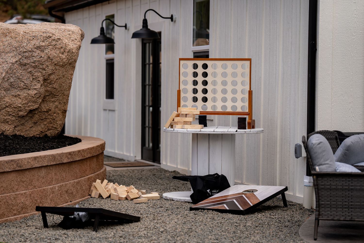 Outdoor seating area with black sconces and wooden game board against white wall.