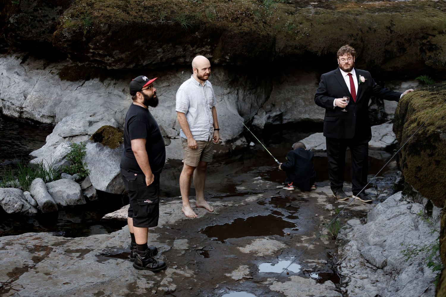 Group explores rocky riverbed terrain during outdoor wedding photo session.