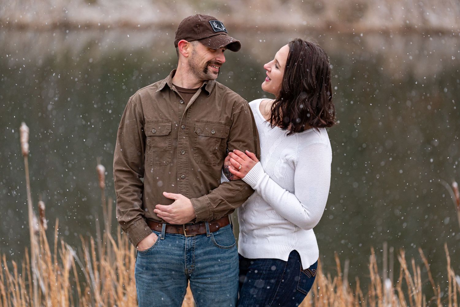 Couple shares intimate moment in field during winter engagement photo session.