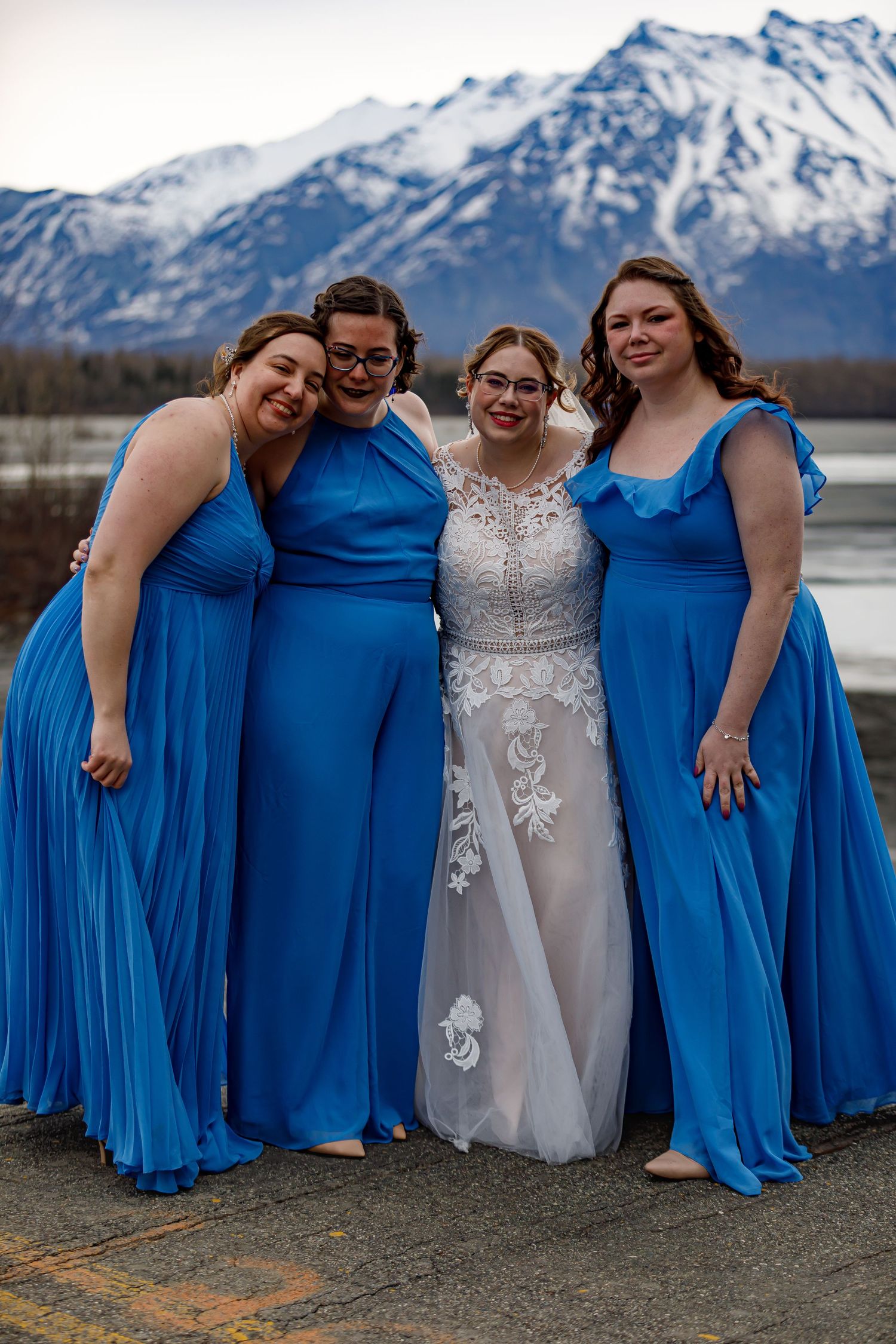 Bridesmaids in bright blue dresses pose with the bride against a mountain landscape.