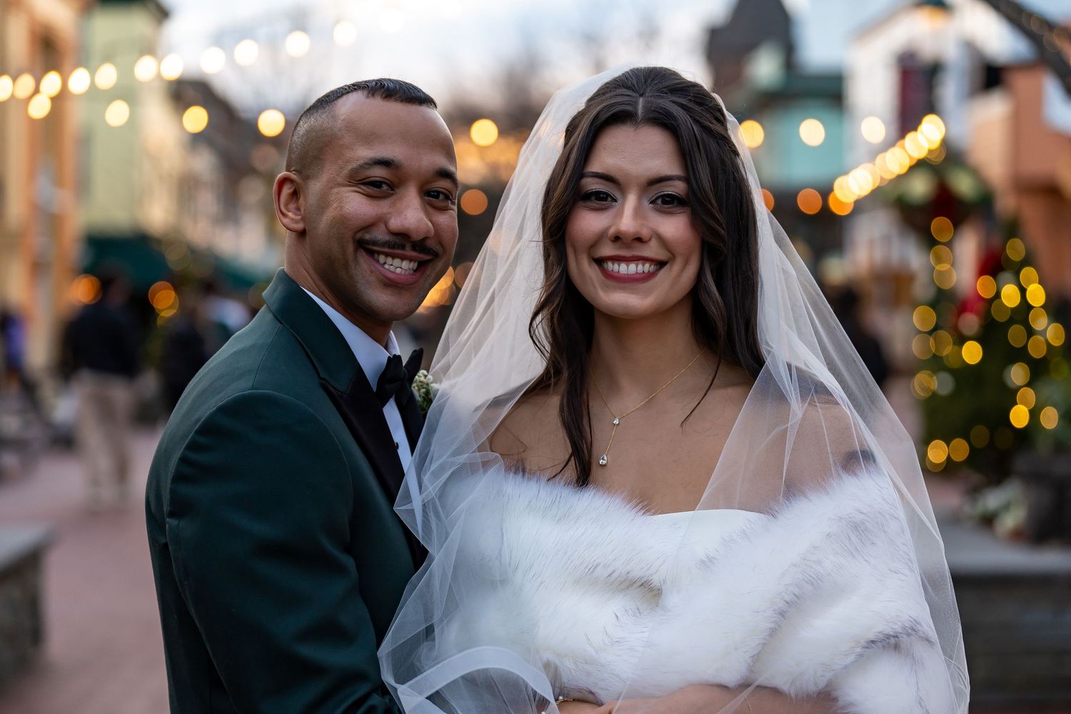 Wedding couple shares joyful moment with festive lights in background.