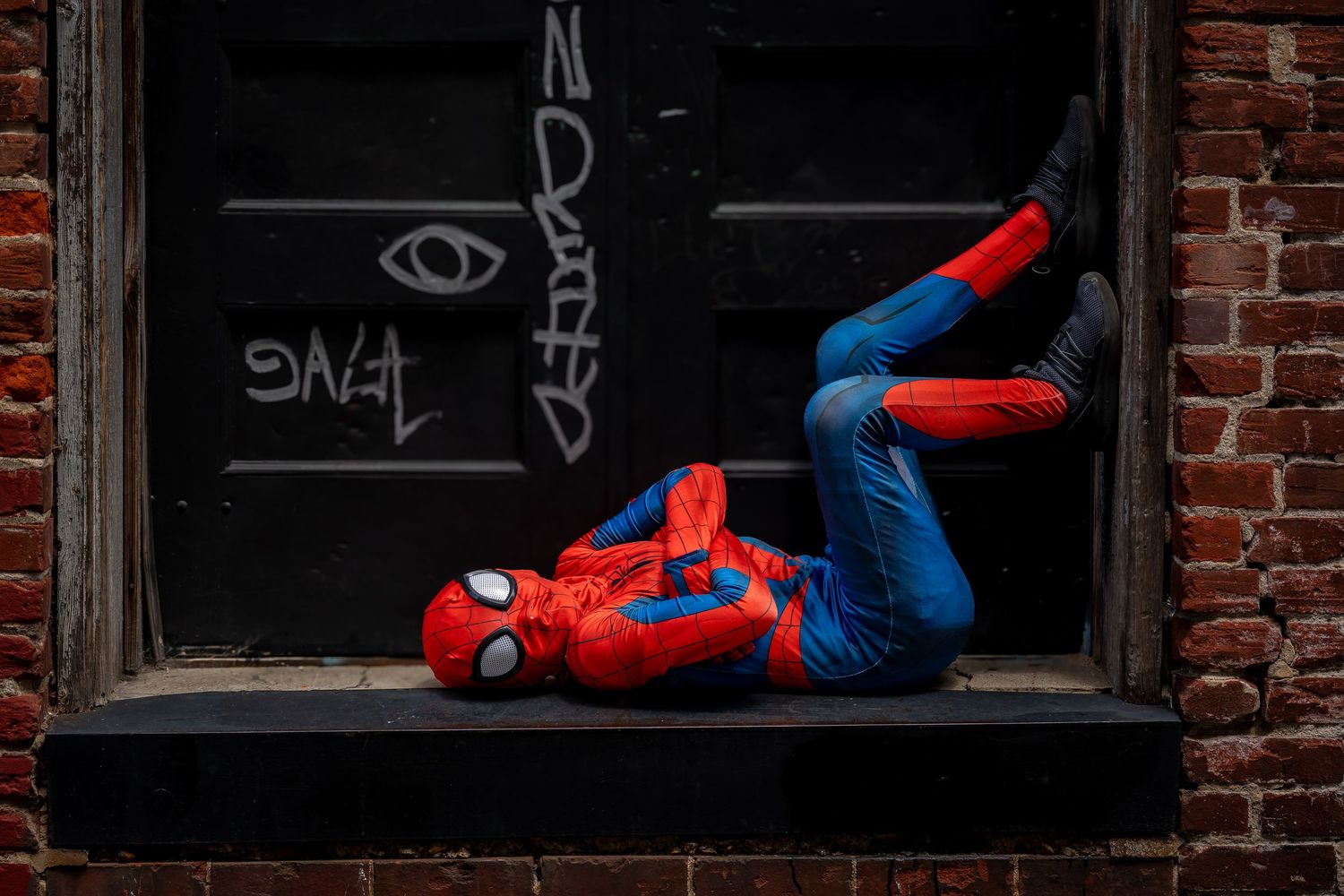 Spider-Man cosplayer performing acrobatic poses near brick buildings.