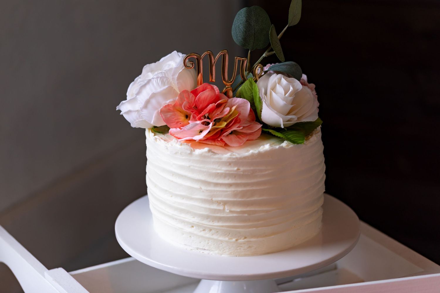 White wedding cake with textured frosting and coral flower decorations displayed on a cake stand.
