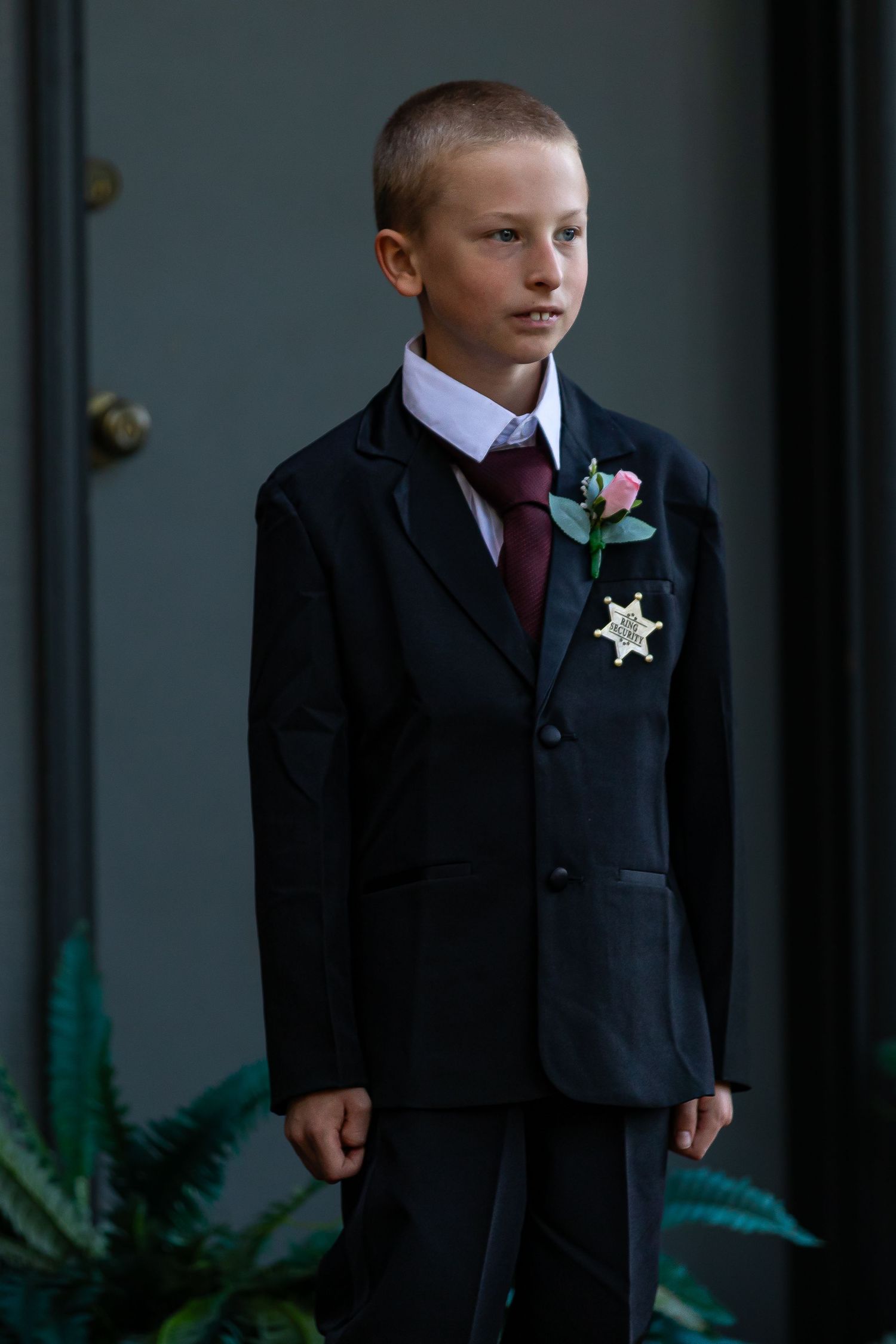 Young attendants in dark suits with burgundy ties stand formally during a wedding ceremony.