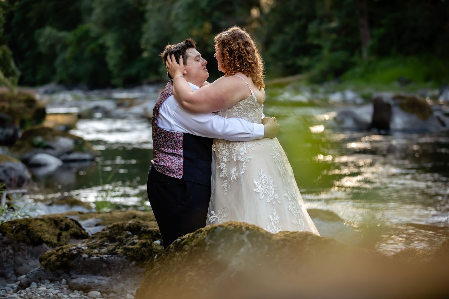 Wedding couple shares intimate moment by scenic forest stream.