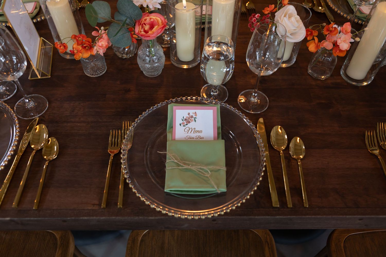 Elegant rustic wedding reception table with gold flatware and orange floral accents.