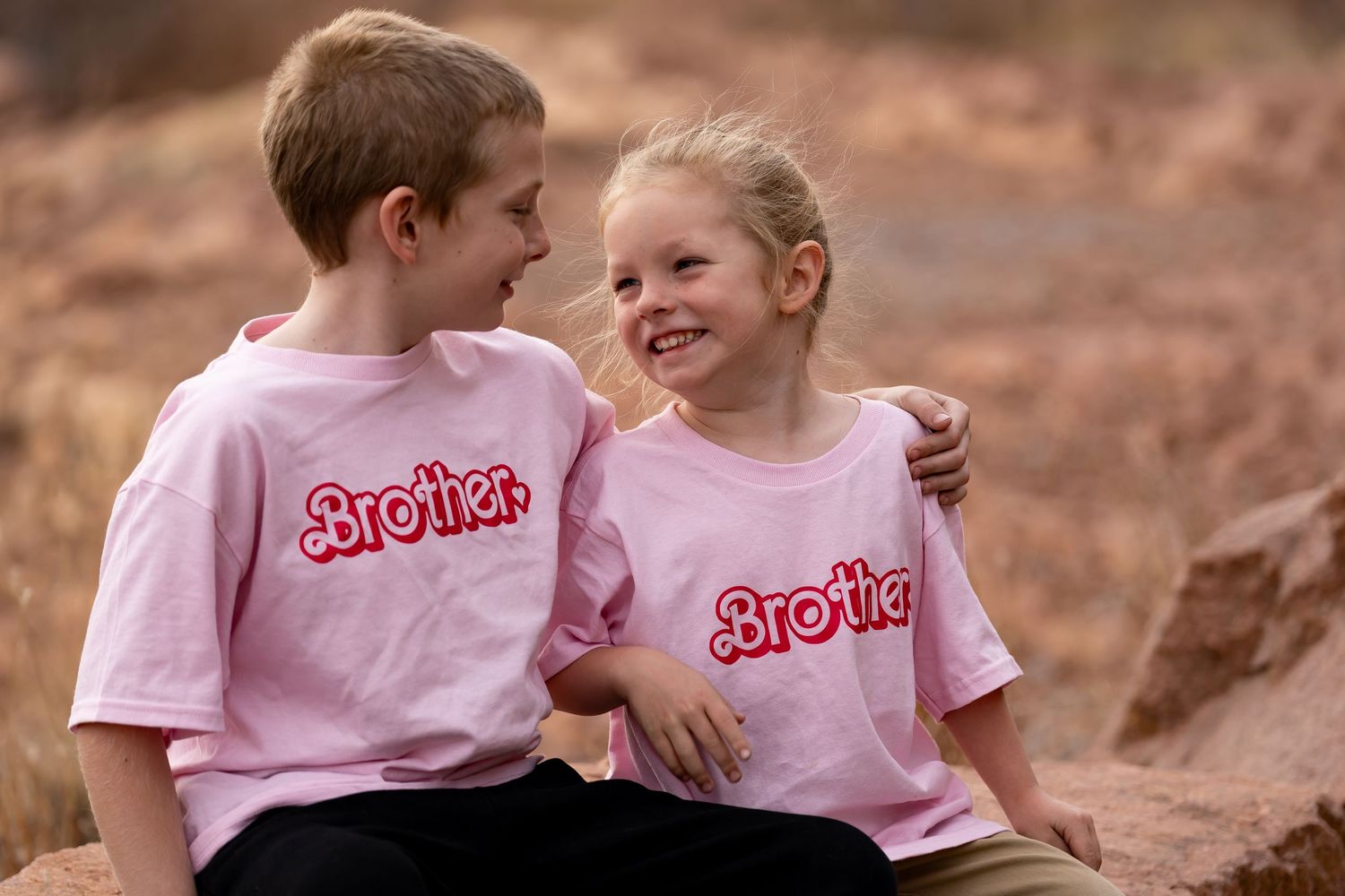 Children in matching pink shirts play together on red rock formations.