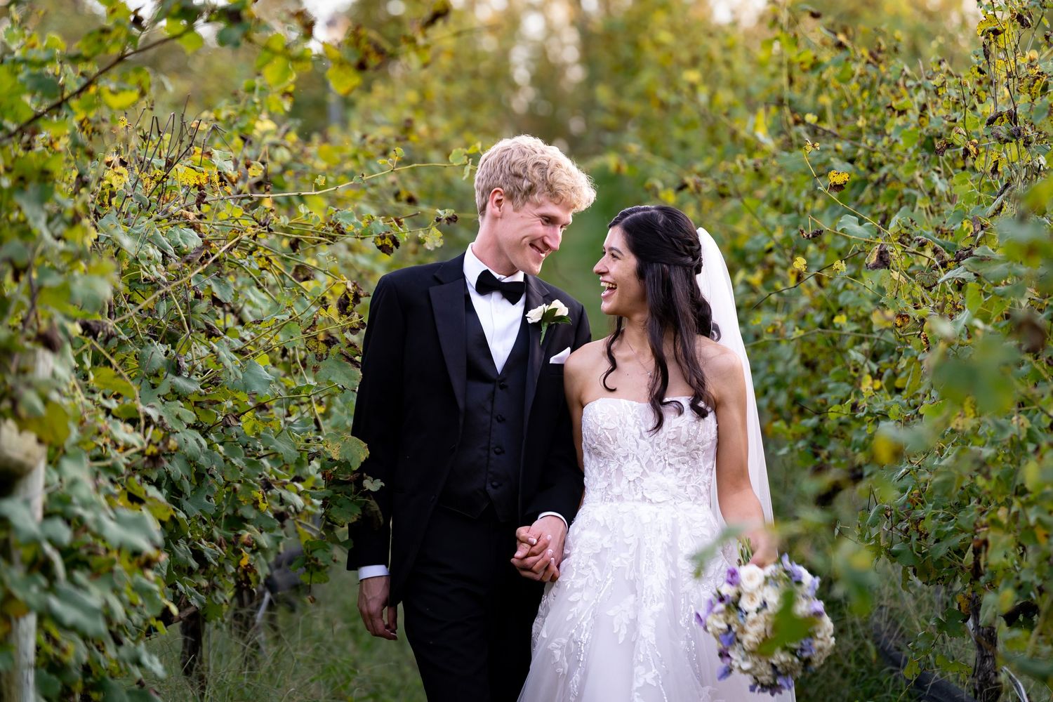 Newlyweds share a candid moment while walking through a lush garden setting.