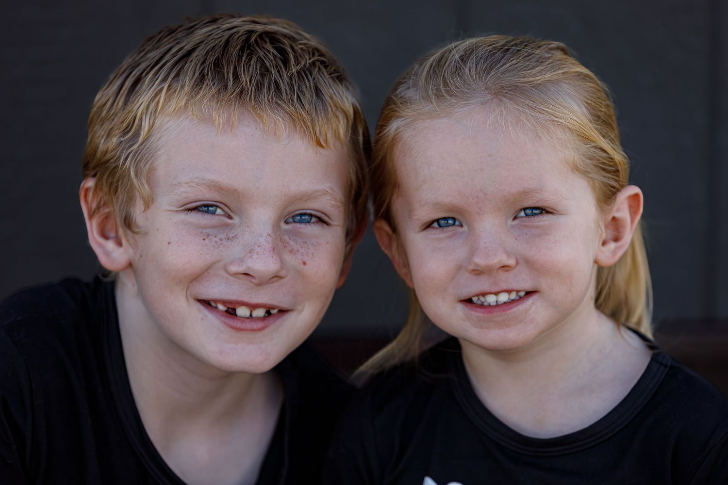 Two siblings wearing matching black shirts pose together for a heartwarming portrait.