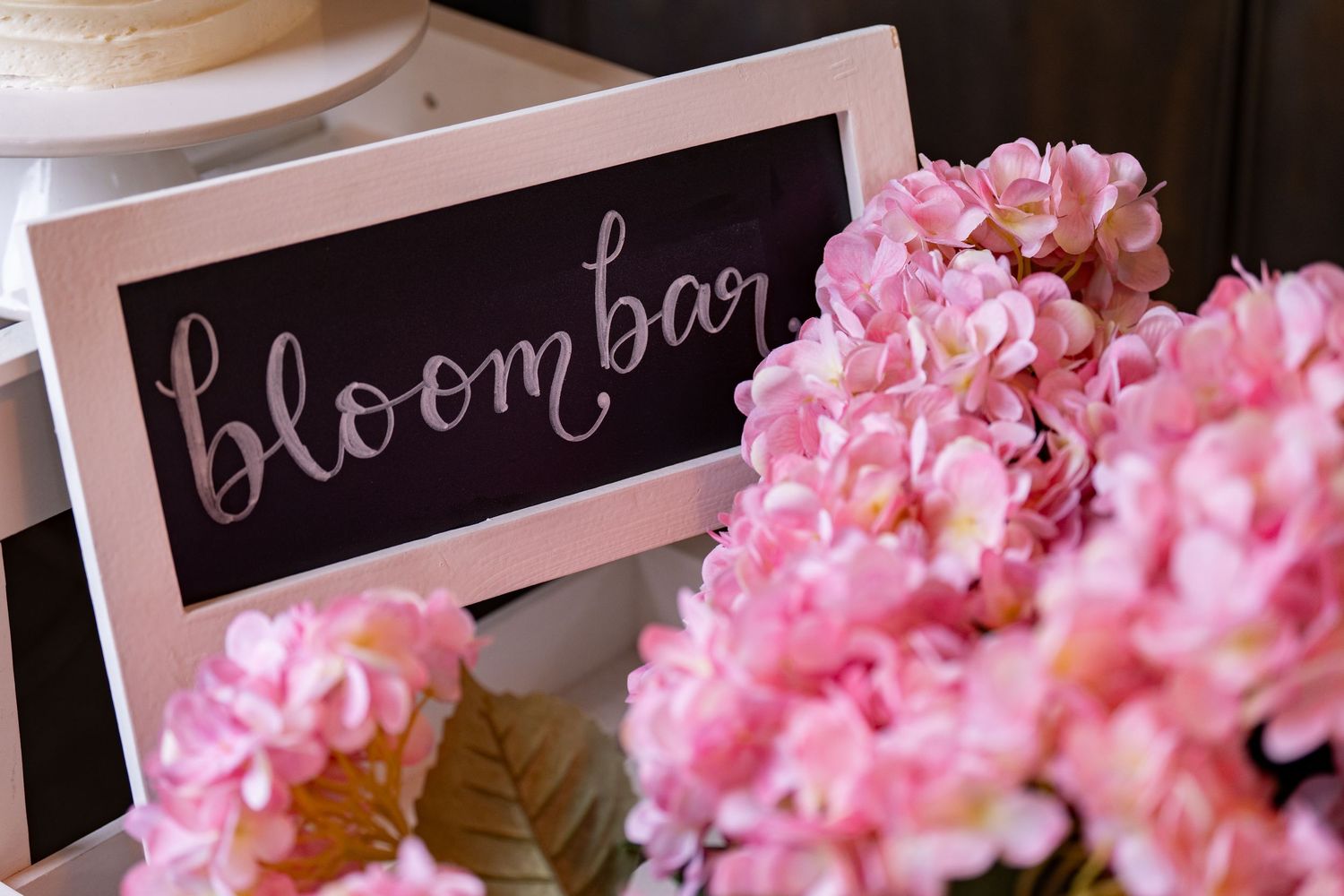 Pink hydrangeas next to a chalkboard sign reading 'bloom' in cursive lettering.