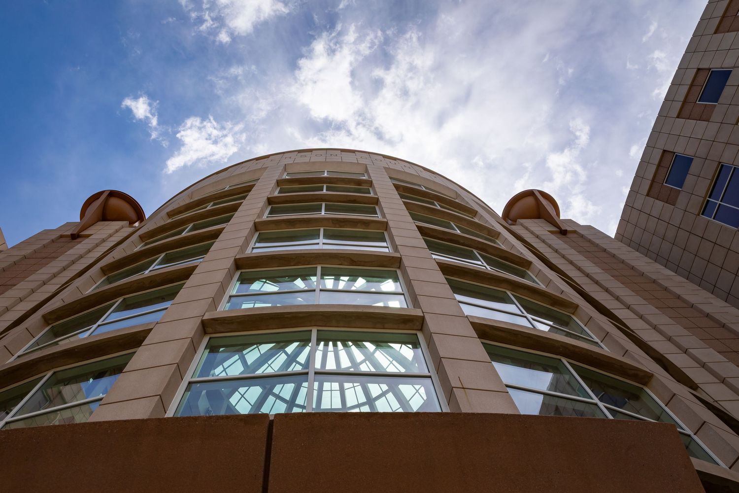 Looking up at curved architecture and windows of modern building facade against blue sky.