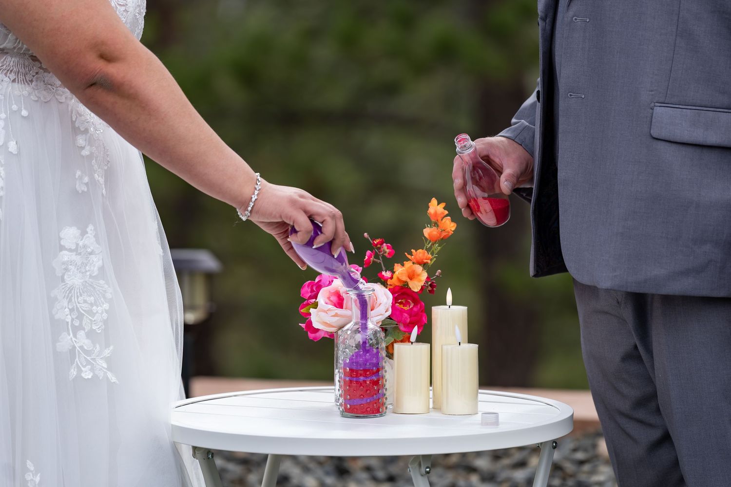 Couple performing unity candle ceremony during outdoor wedding.