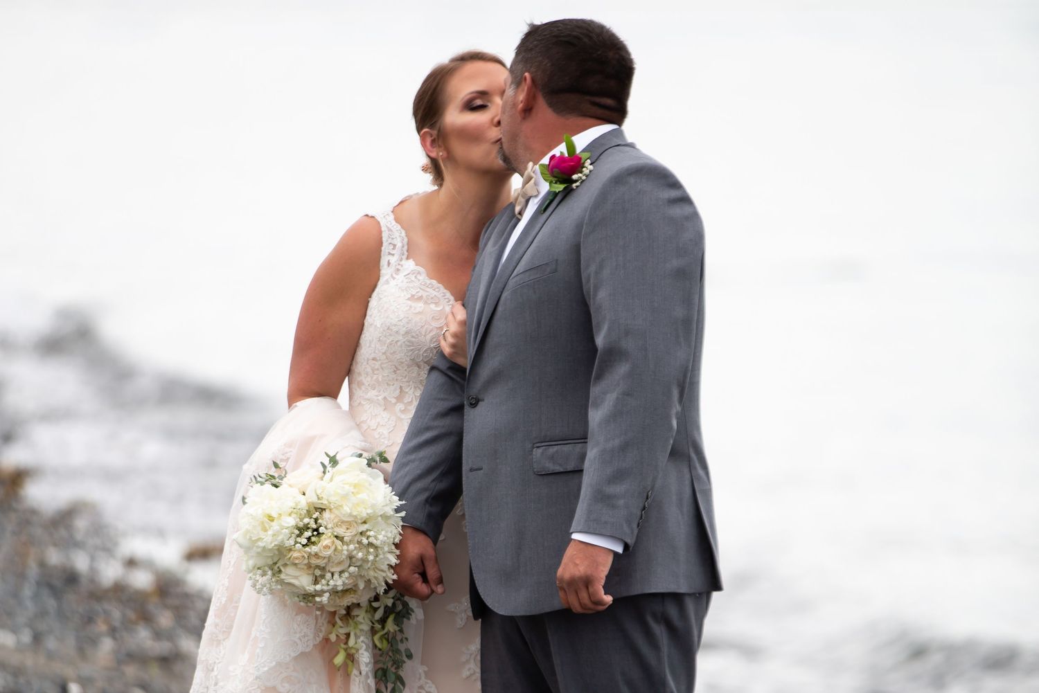 Newlyweds embrace against a white background in formal wedding attire.