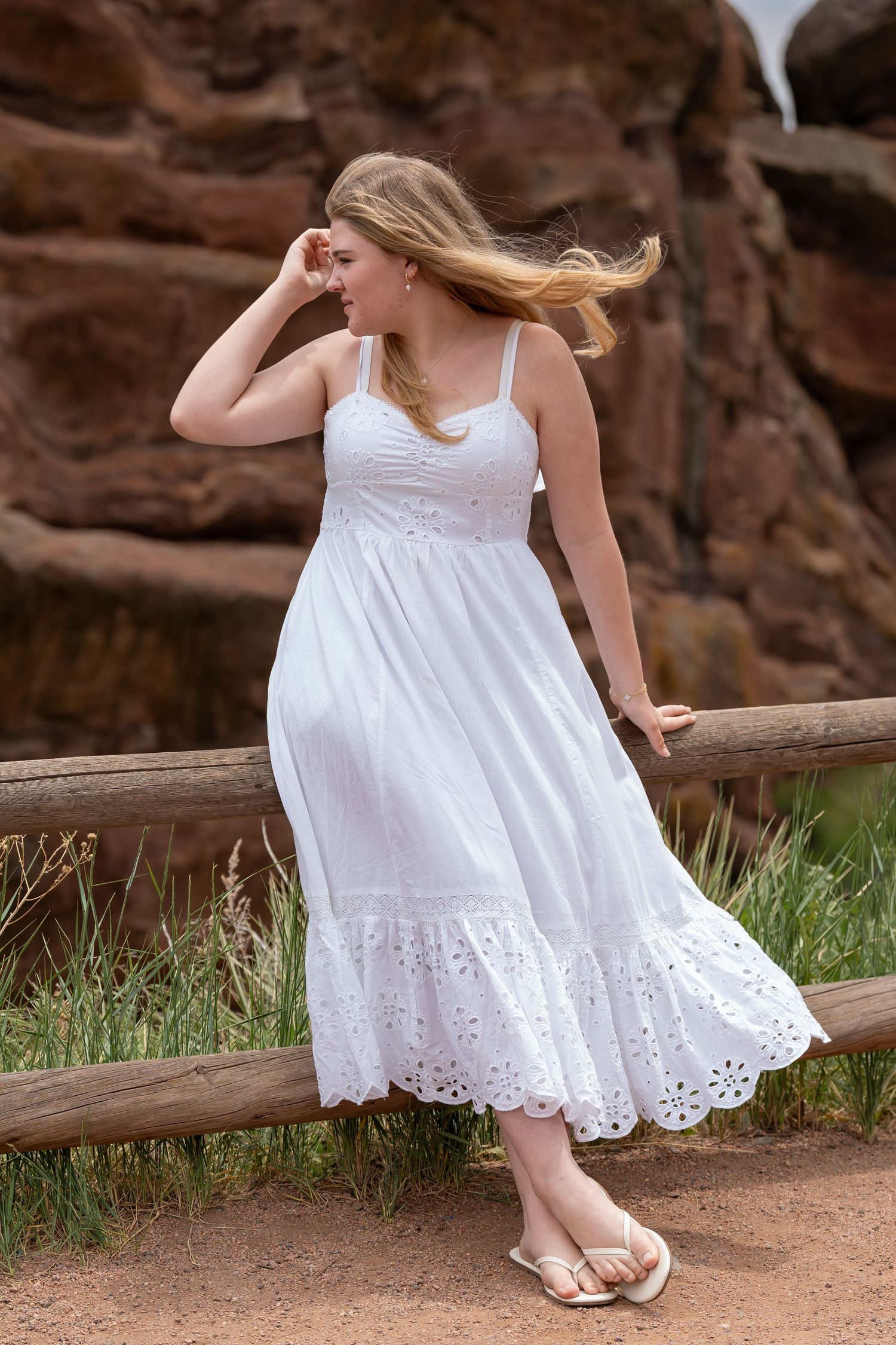 A flowing white eyelet lace dress catches the breeze against red rock formations in an outdoor setting.