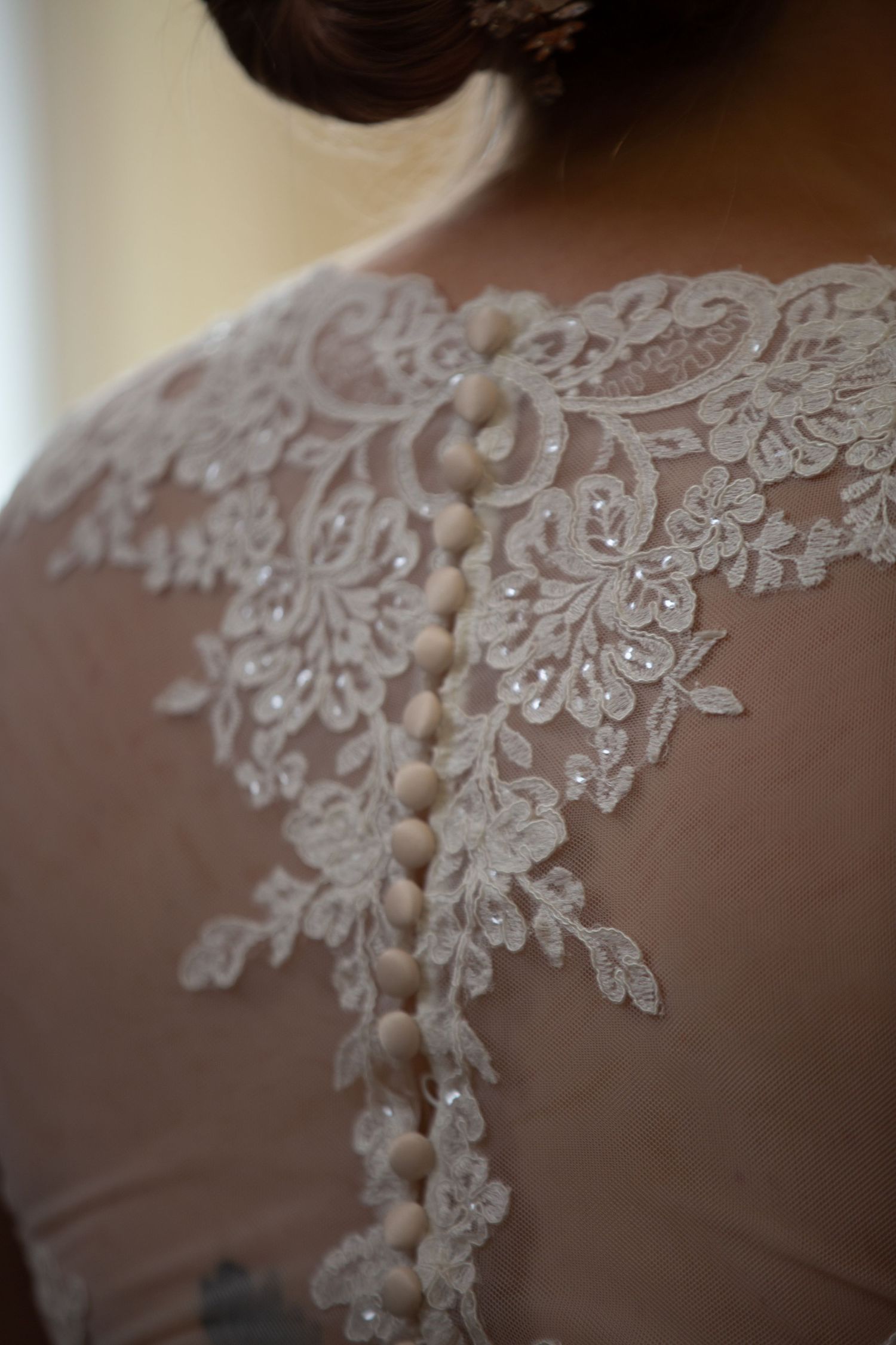 Detailed view of intricate white lace applique and button closures on sheer wedding dress fabric.