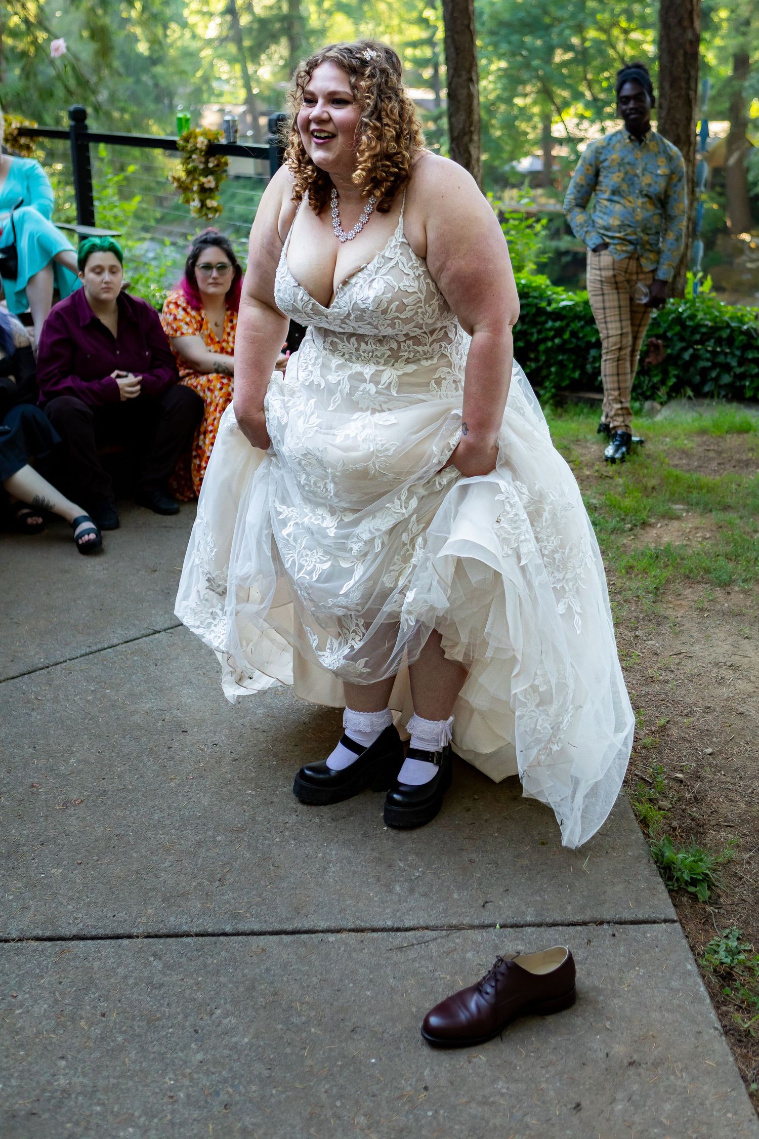 Close-up of a white lace wedding dress and shoes on a concrete pathway.