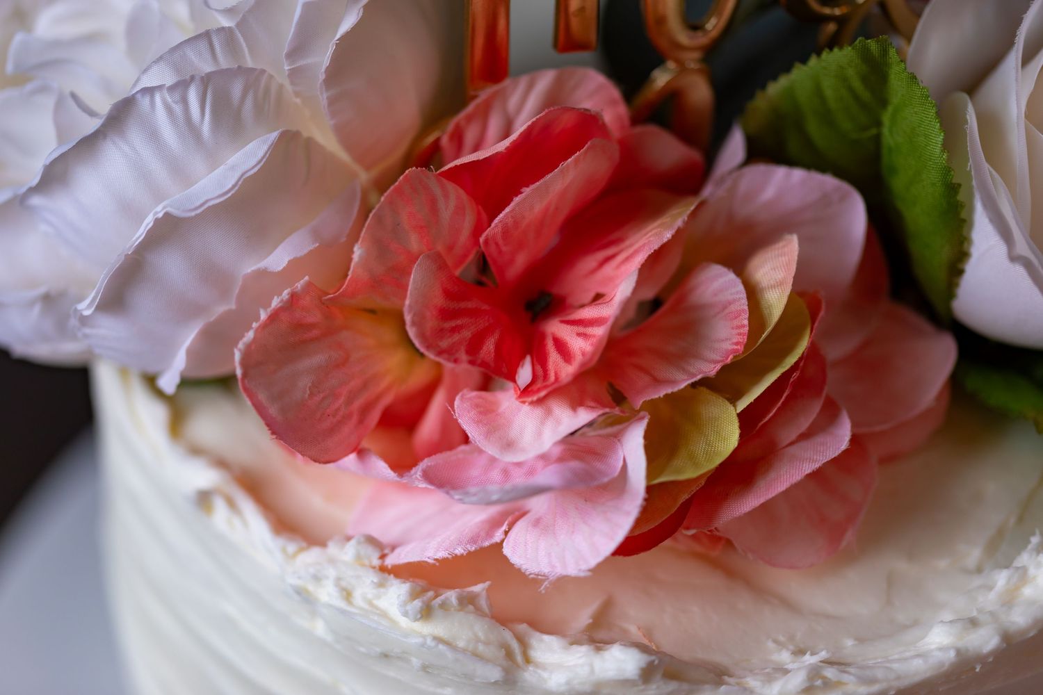 Close-up of pink and coral flowers adorning a white wedding cake.