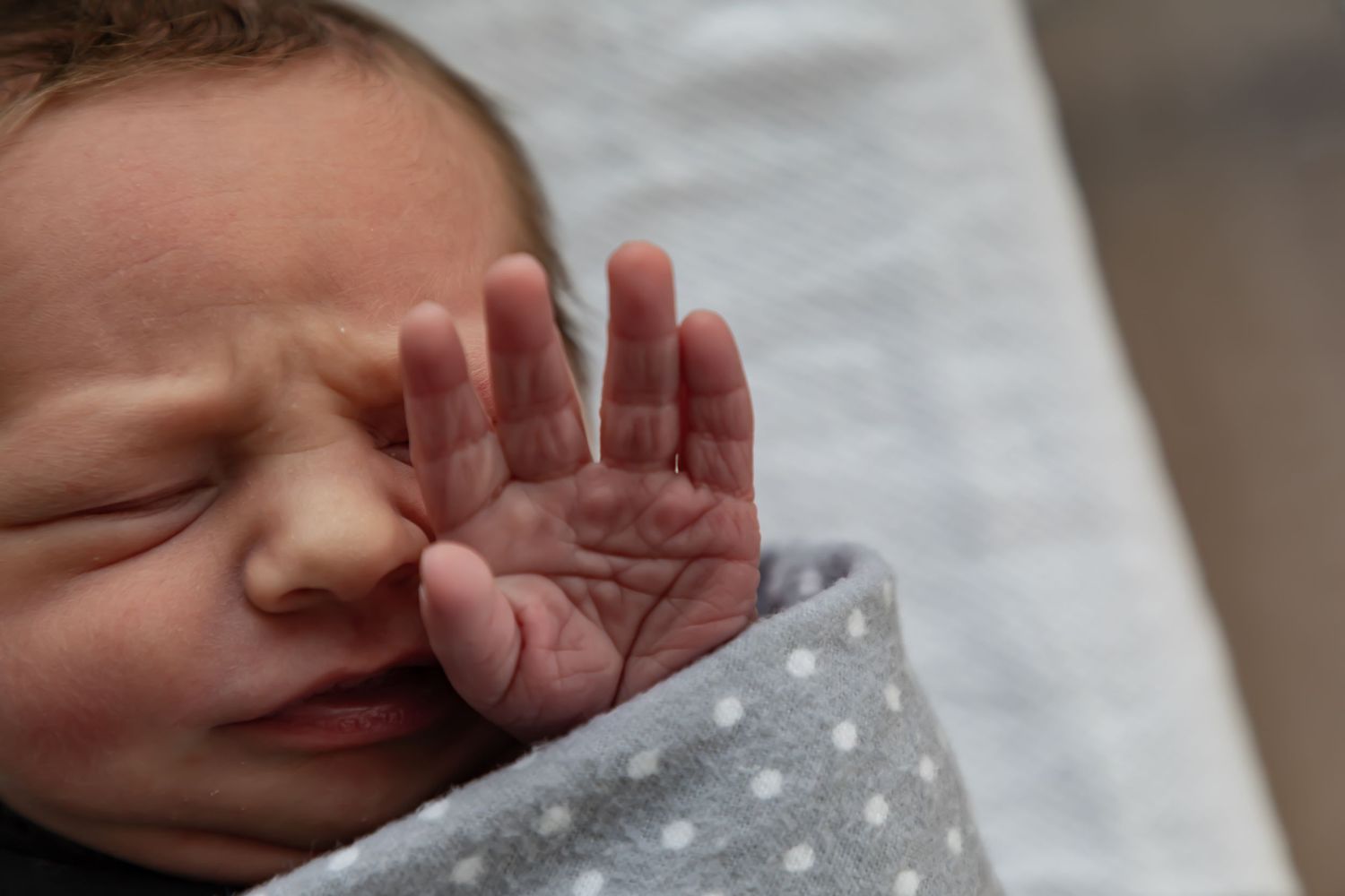 Close-up of a sleeping newborn baby boy wrapped in a polka dot blanket in the hospital during a Fresh 48 session.