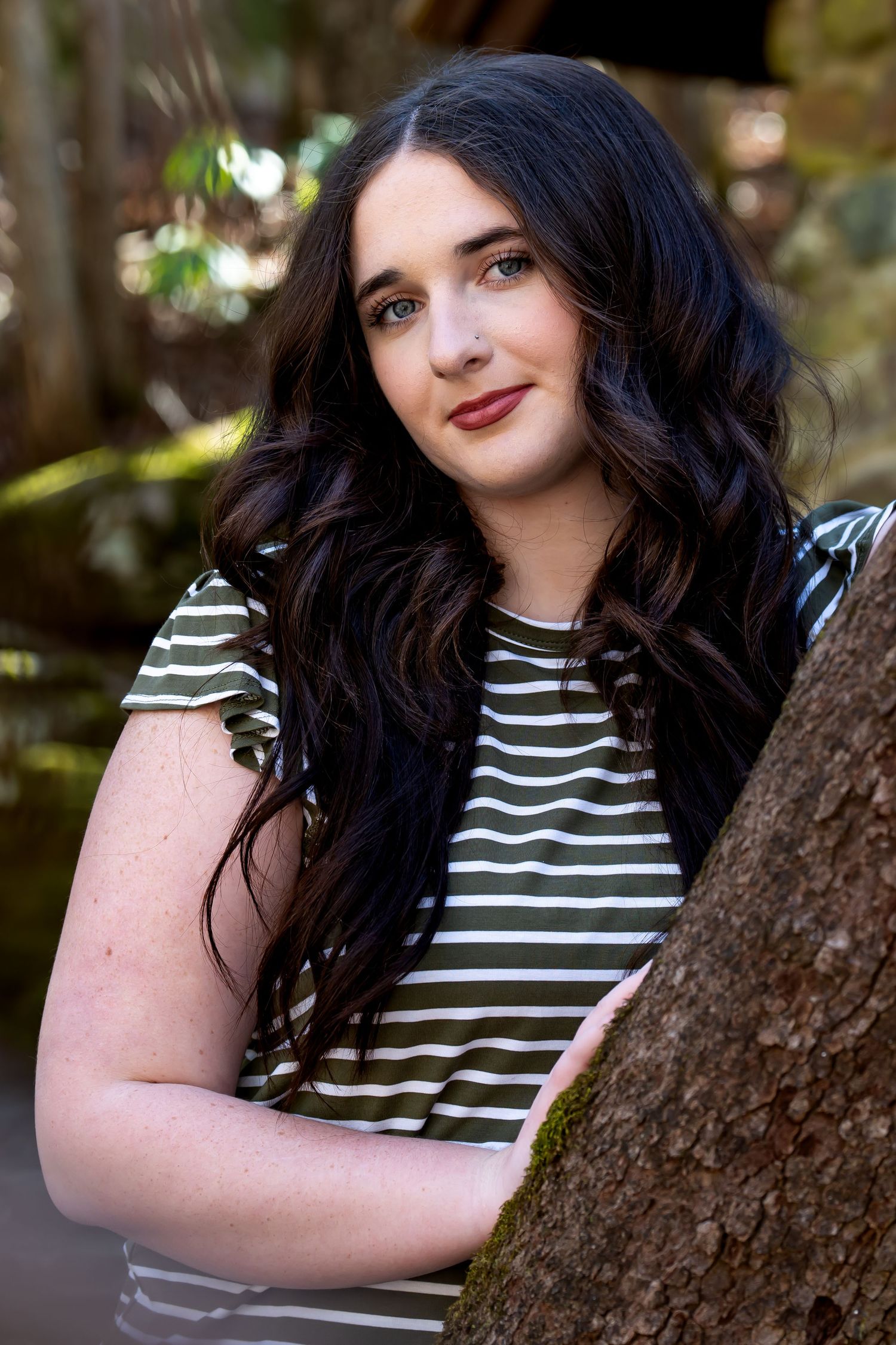 Casual portrait session featuring striped top and natural poses against tree backdrop.