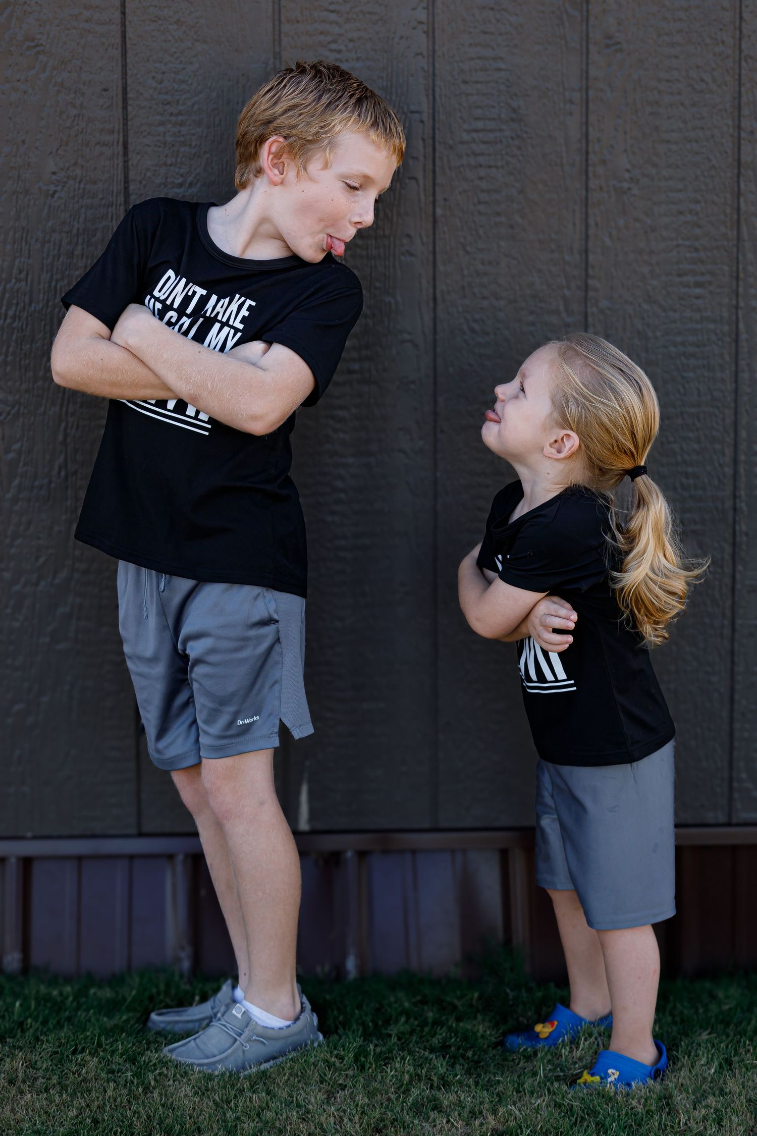 Two children in matching outfits stand with crossed arms in a playful standoff pose.