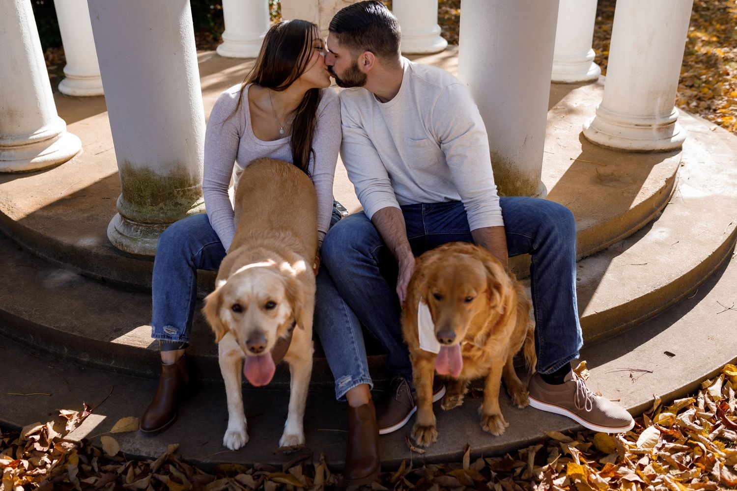 Casual outdoor portrait session with pets among white columns and fallen leaves.