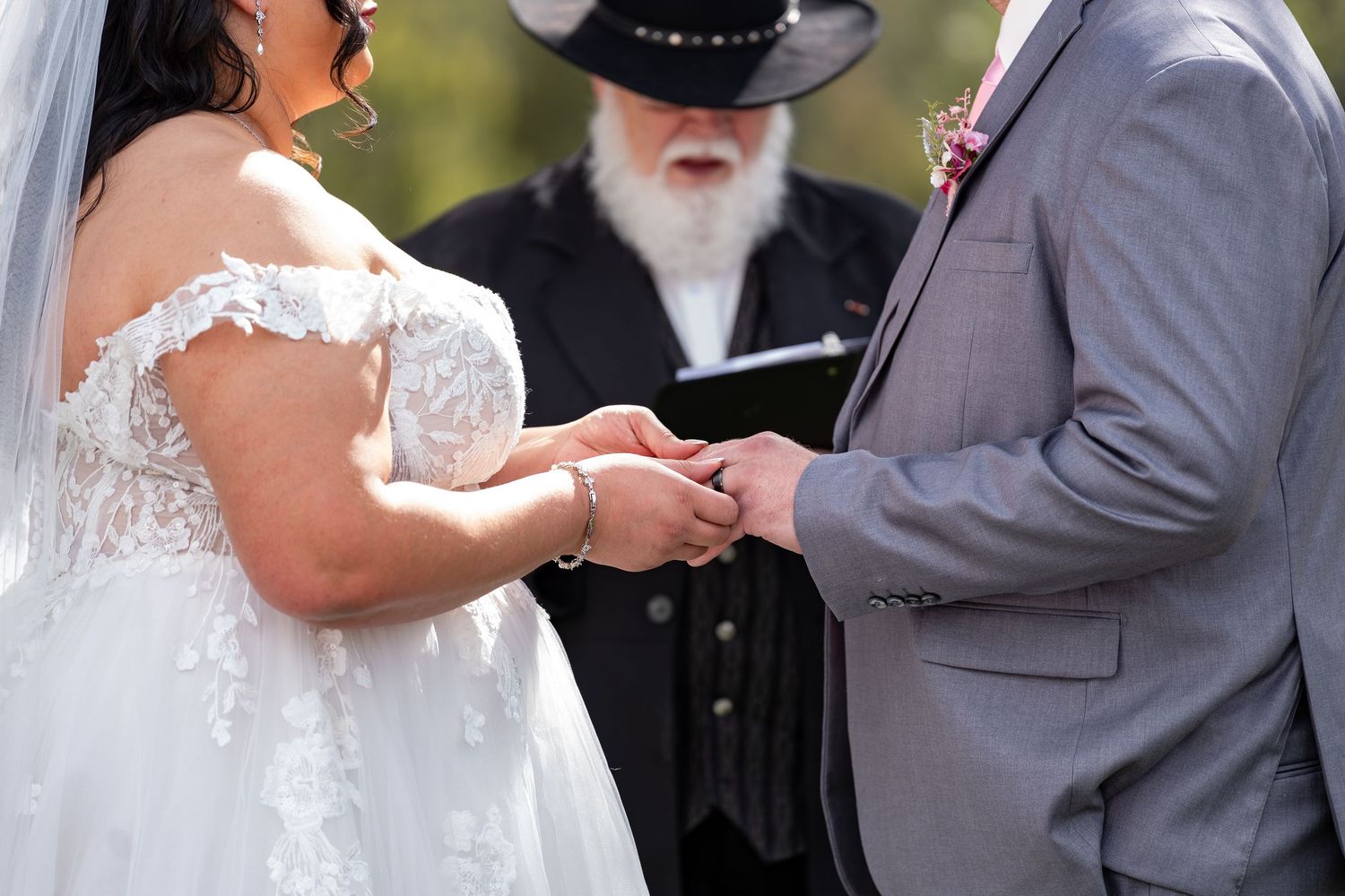 Wedding ceremony participants stand in formal attire near decorative floral arrangements.