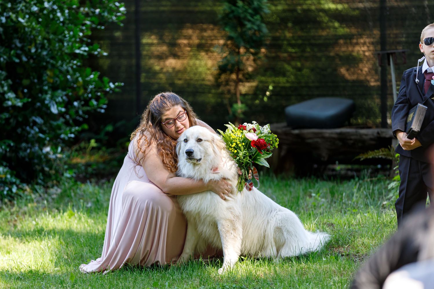 A wedding party member pets a friendly white dog during an outdoor photo session.