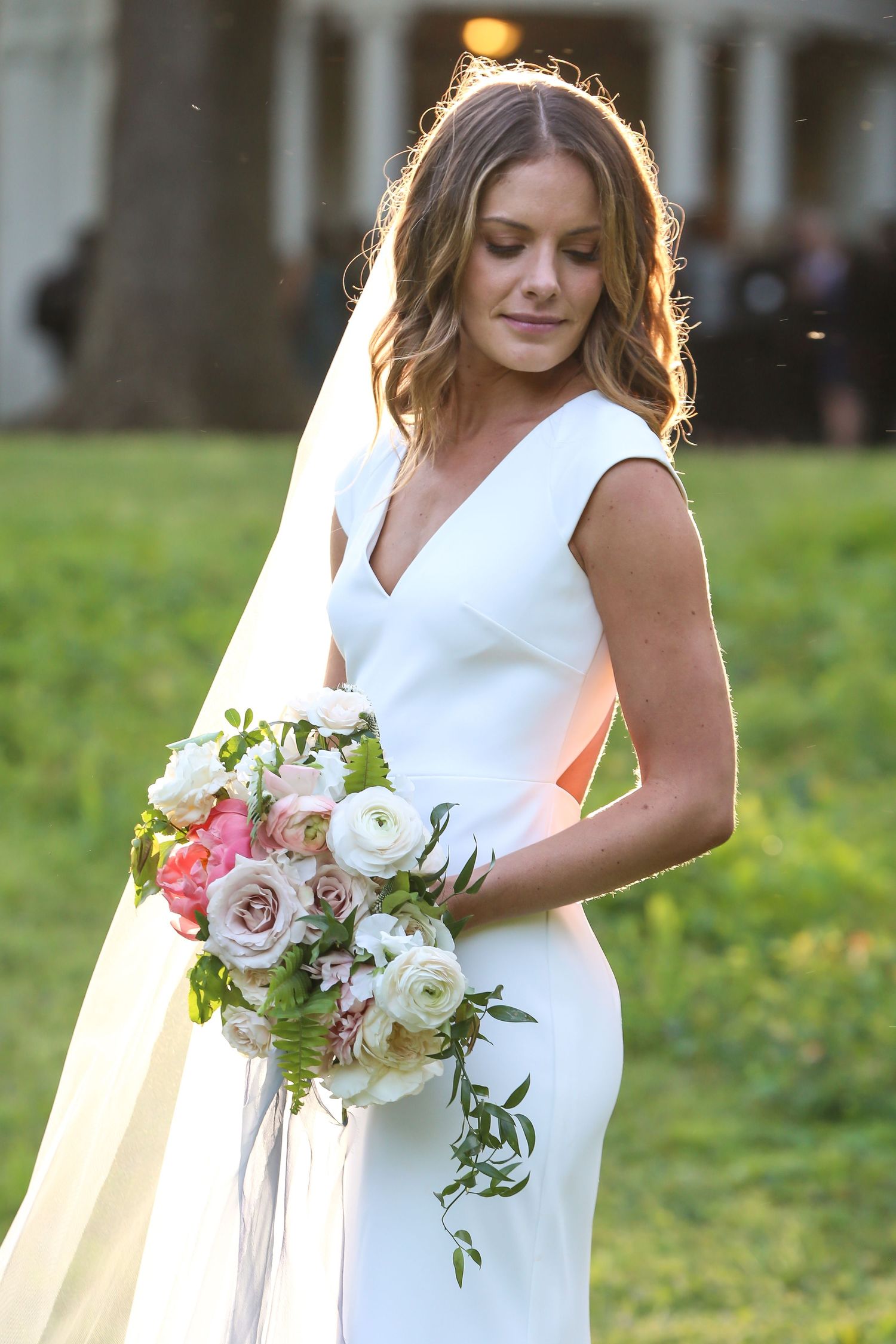 Elegant white wedding dress and floral bouquet details in outdoor garden setting.
