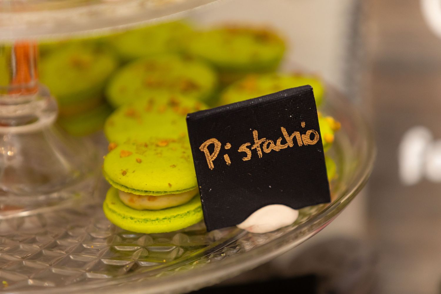 Close-up of pistachio-flavored green macarons on a glass display stand with black label.