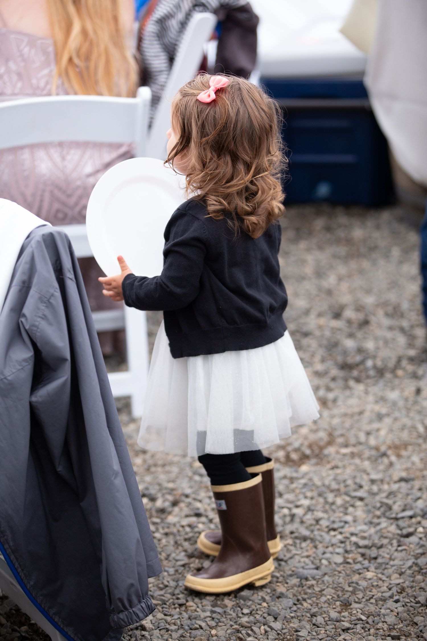 Details of wedding attire showing white dress and rain boots on gravel ground.