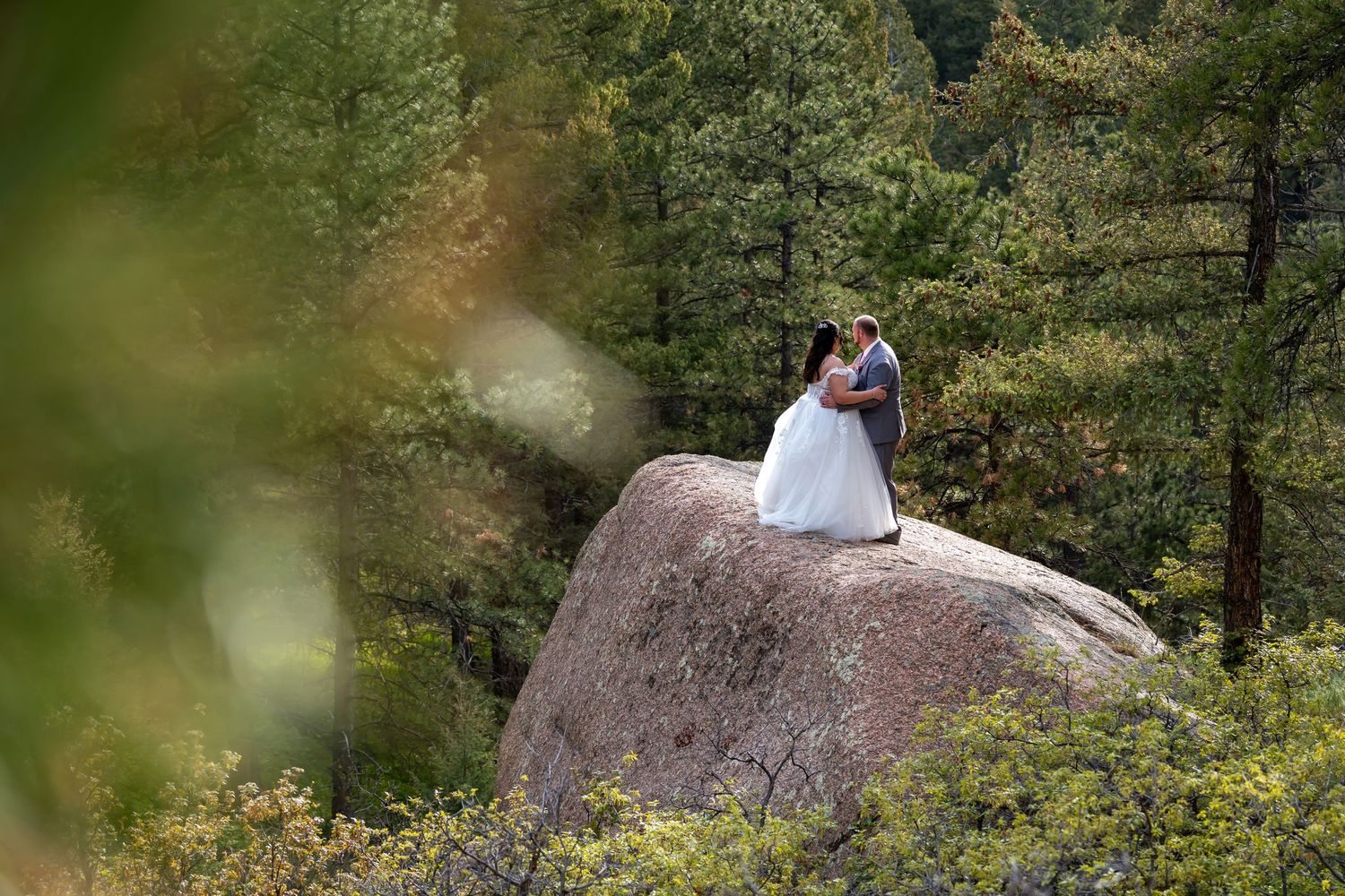 Wedding photography on a rocky mountain overlook surrounded by pine trees and natural scenery.