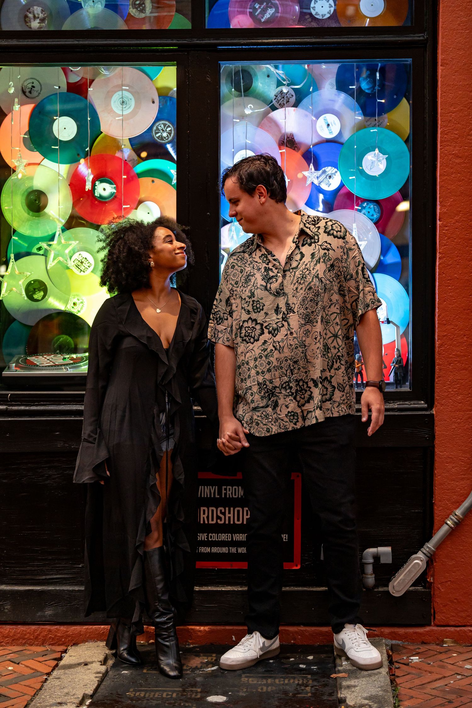 Couple standing in front of colorful vinyl record display outside record shop.