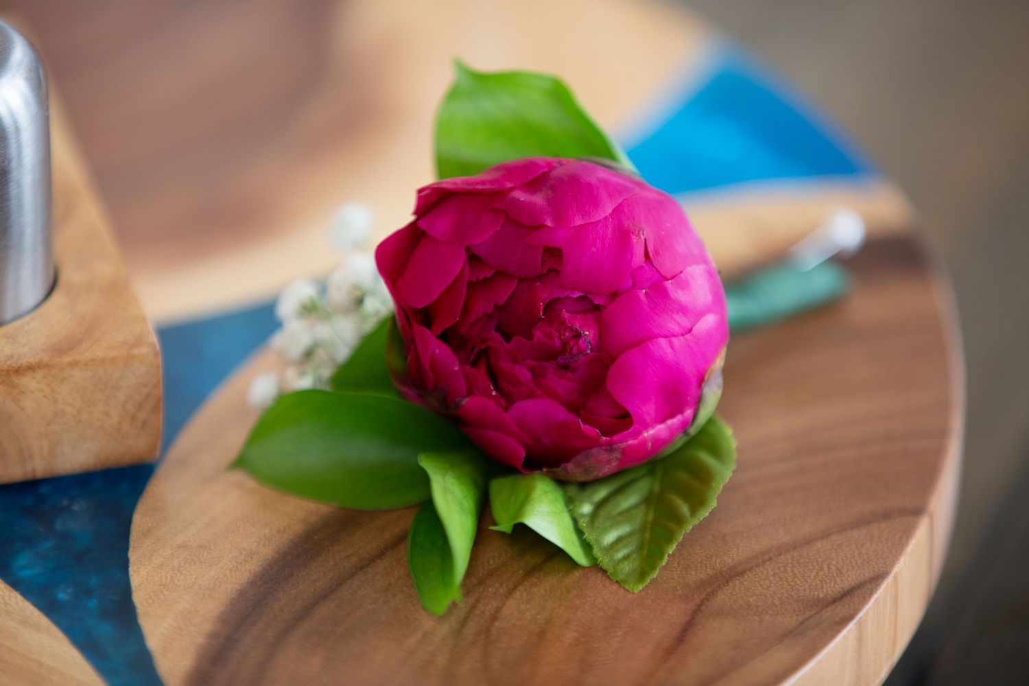 Vibrant pink peony flower displayed on wooden surface with blue accent.