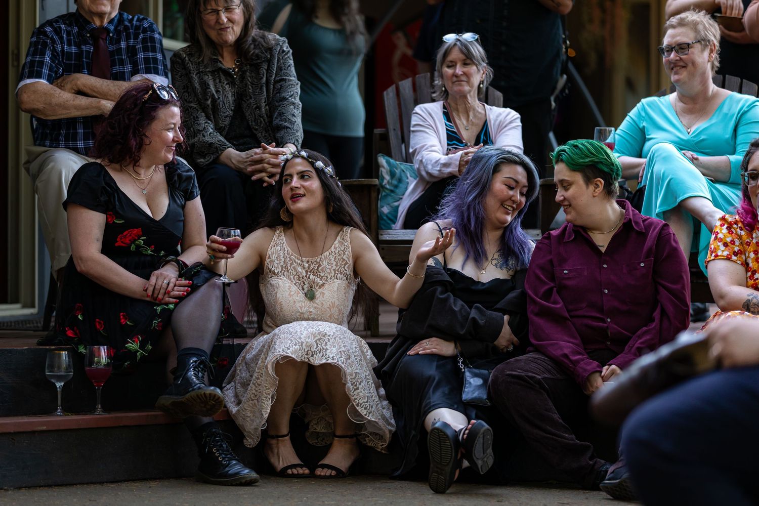 Wedding guests relax on wooden benches during an outdoor celebration.