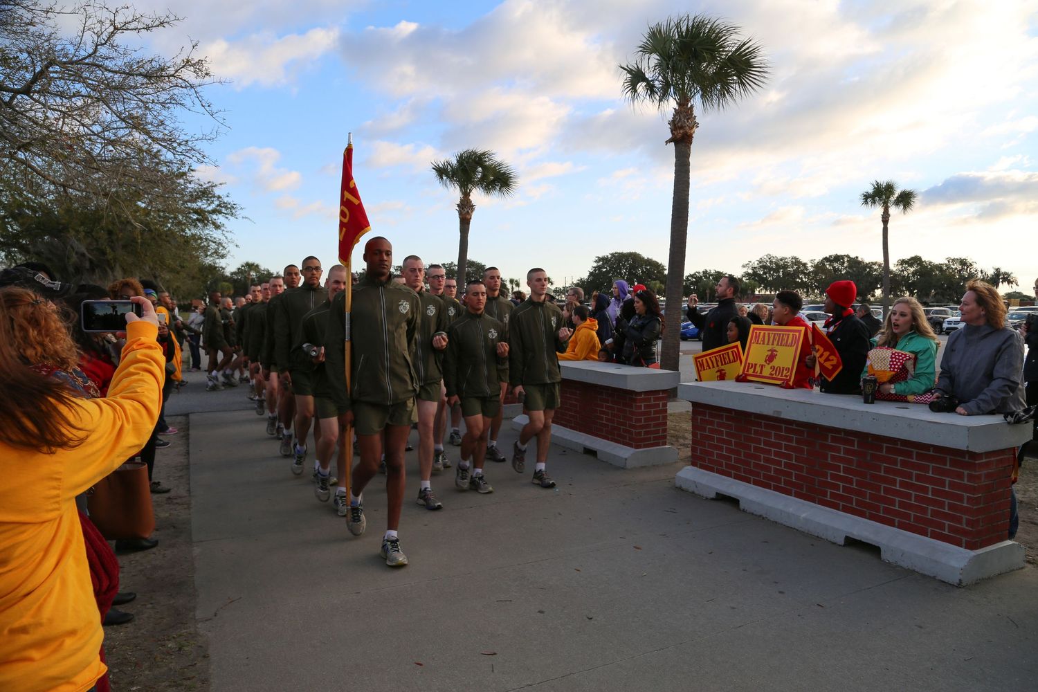 Marine recruits standing in formation at sunset while spectators watch from sidelines.