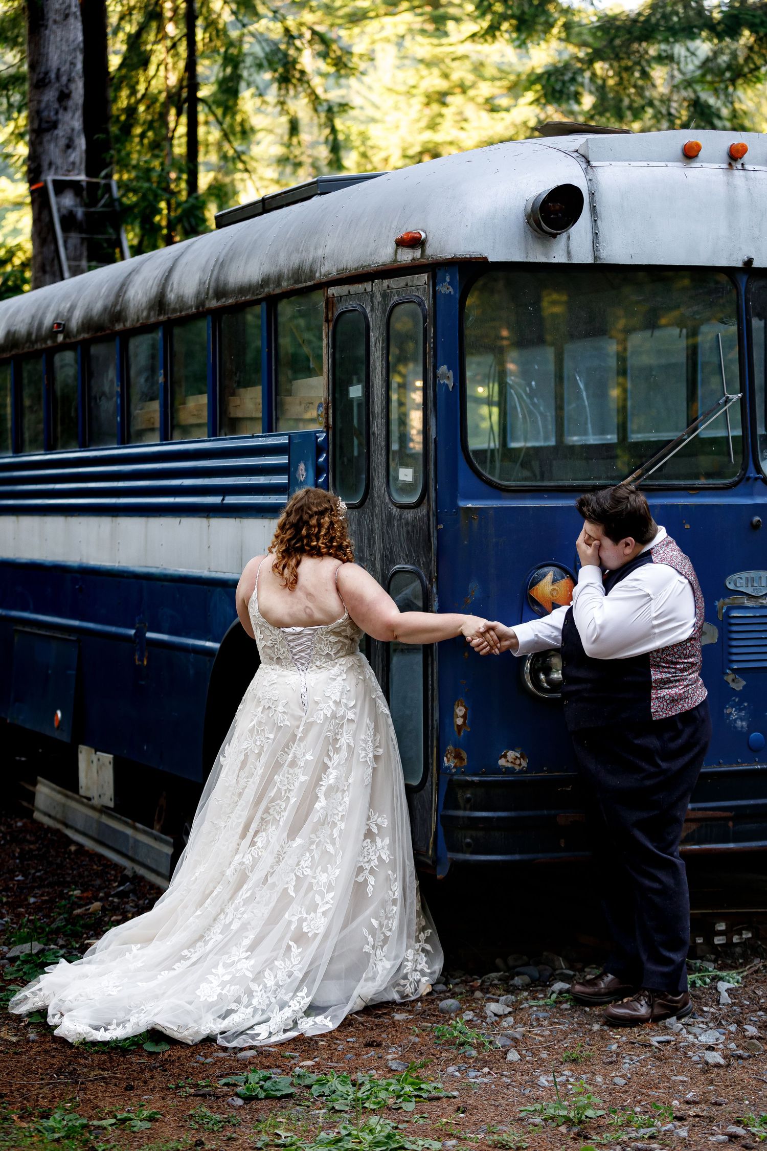 A wedding couple poses playfully in front of a vintage blue bus.