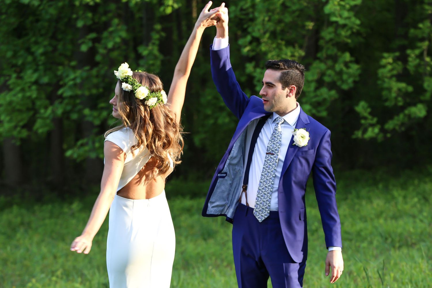 Wedding party in yellow dresses and navy suits poses with pink and white floral bouquets outdoors.