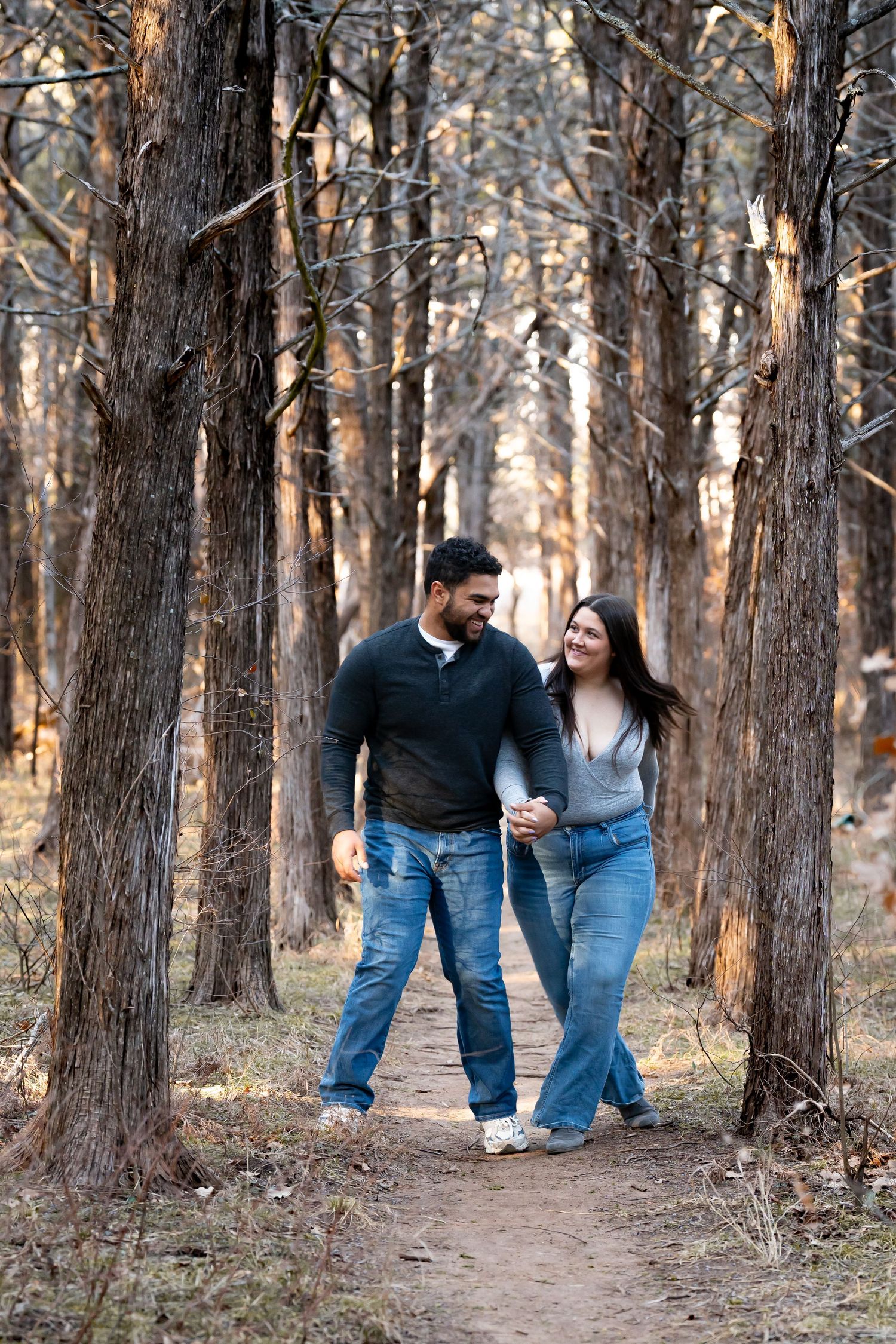 A couple walks together through a scenic wooded forest path wearing matching blue jeans and dark tops.