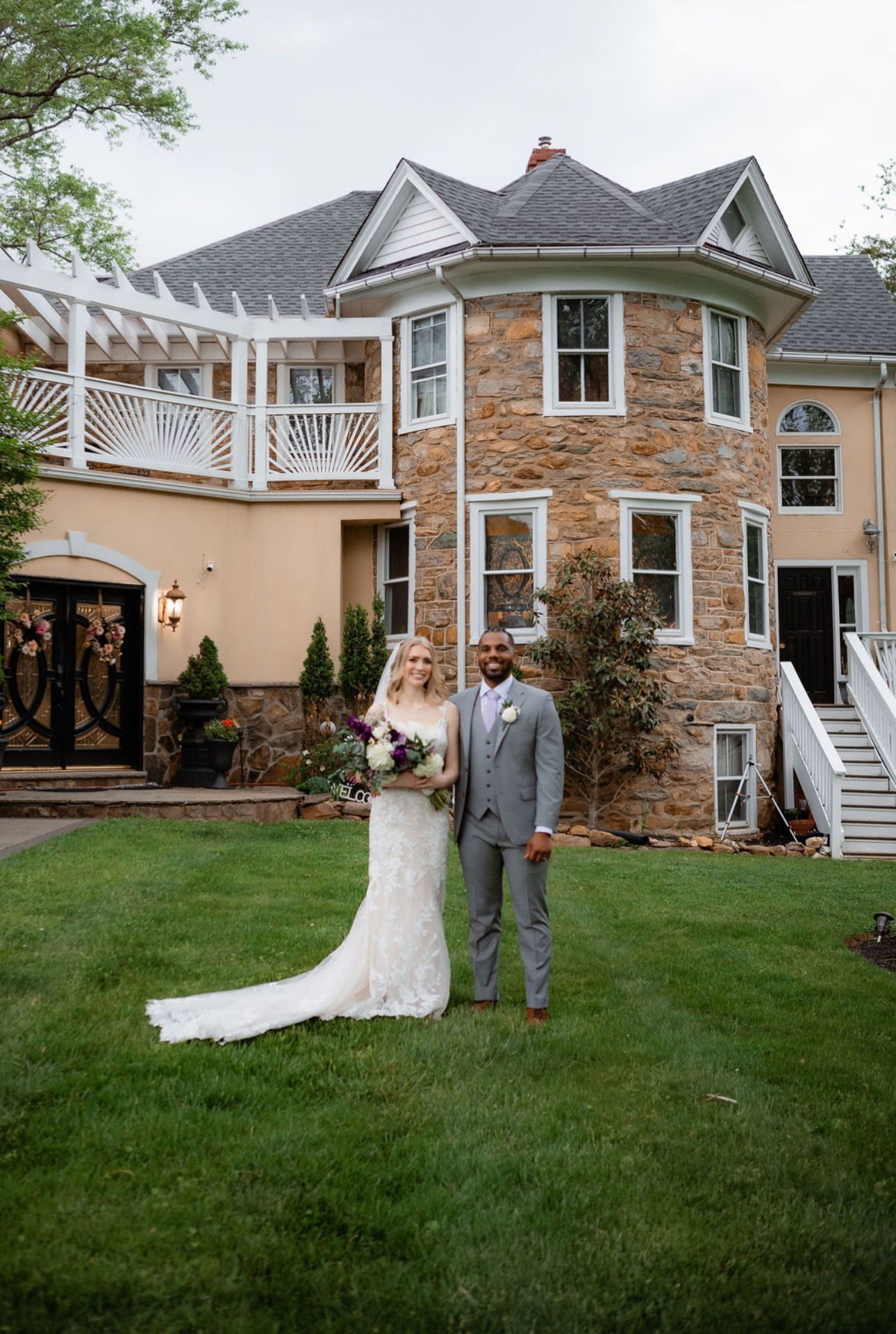 A beautiful wedding celebration at a stone mansion with a turret and deck, featuring a manicured lawn and elegant architecture.