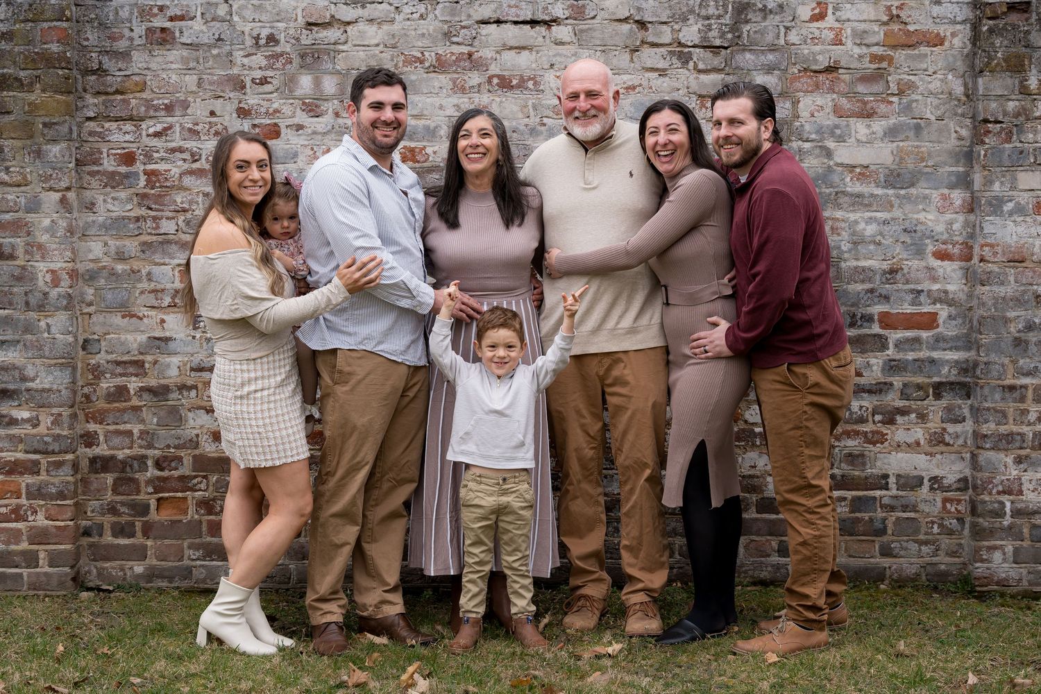 Family group photo session against rustic brick wall in coordinated neutral outfits.