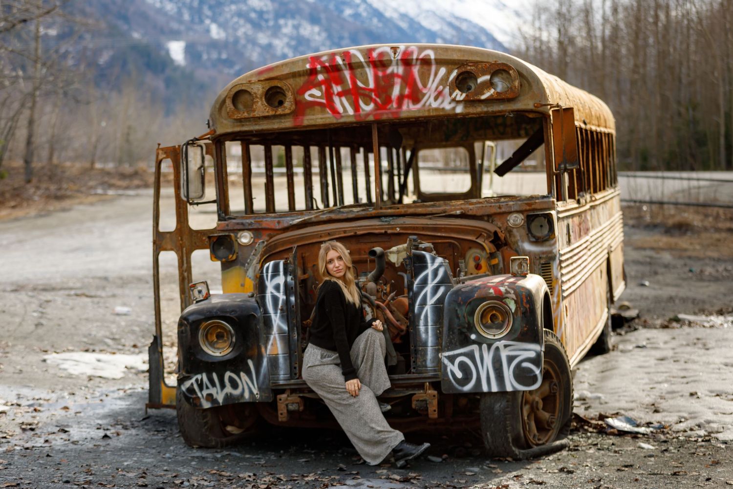 A weathered yellow school bus covered in graffiti sits abandoned in a snowy landscape.