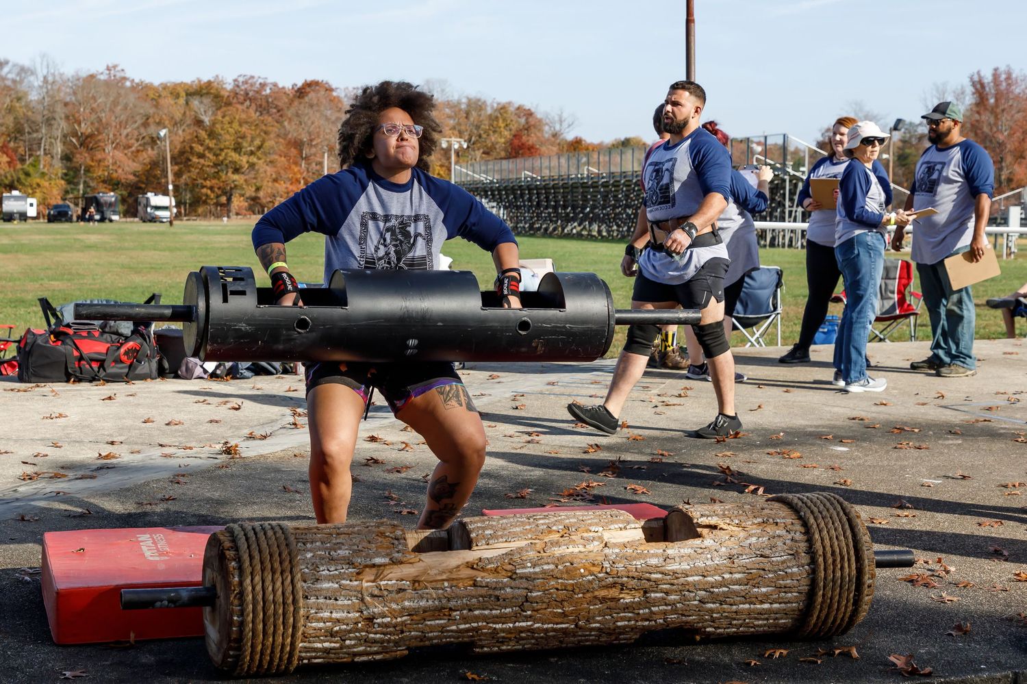 Athletes preparing for log lifting competition on outdoor concrete surface.